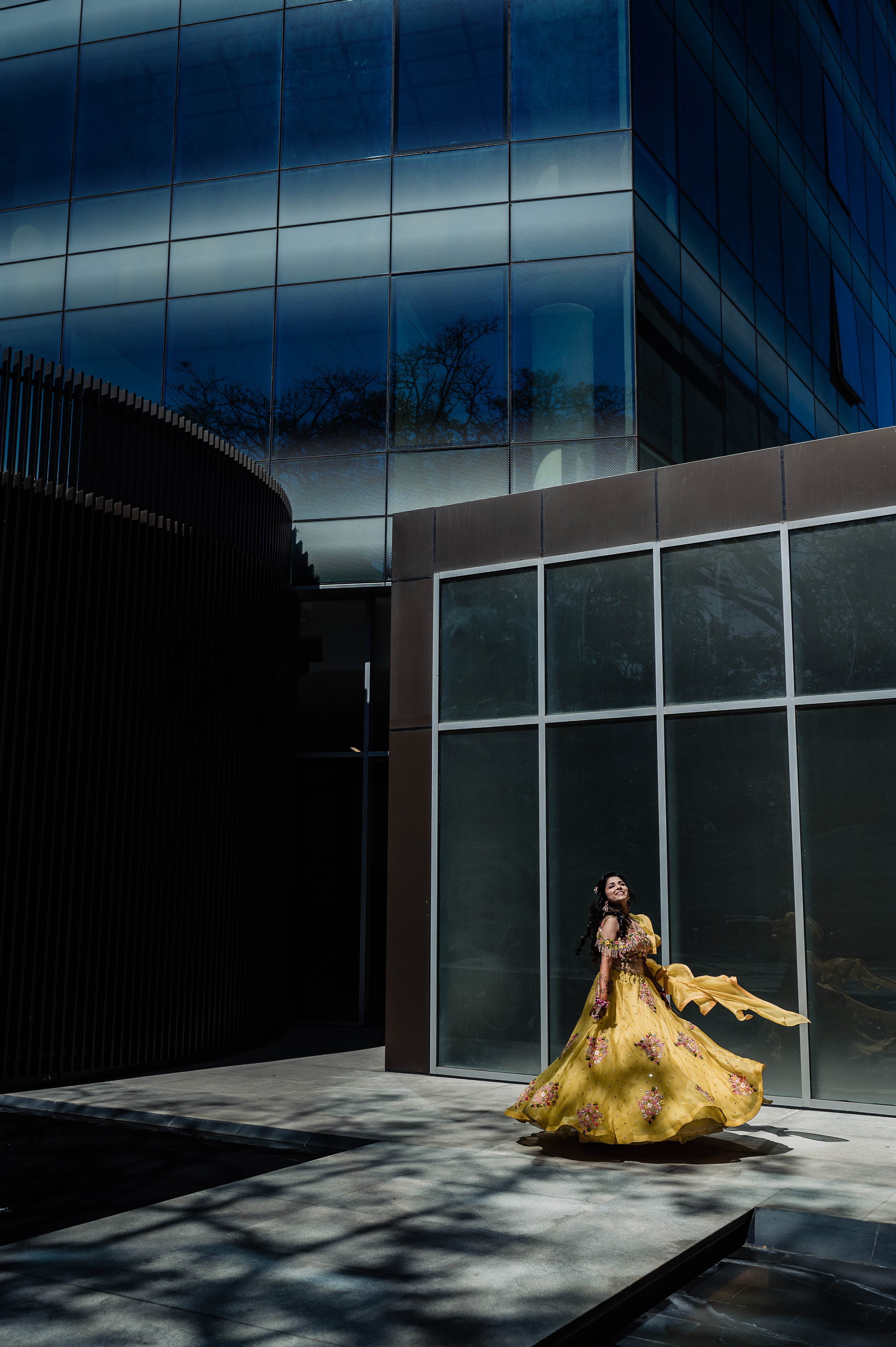 Woman in flowing yellow gown poses against modern glass and metal building facade
