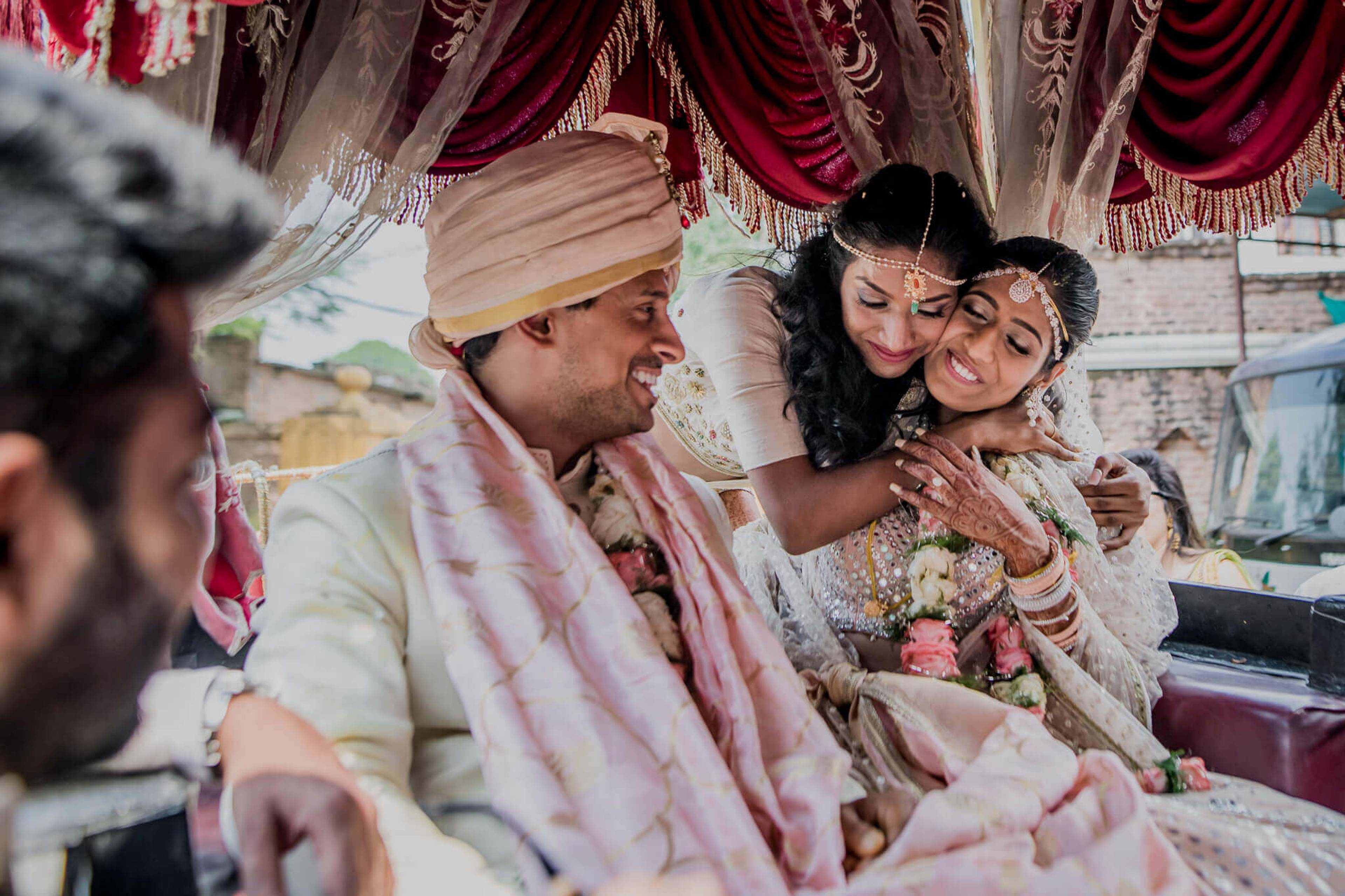 Anu and Raghu smile together under ornate red drapes at their Nepal wedding ceremony, dressed in traditional attire