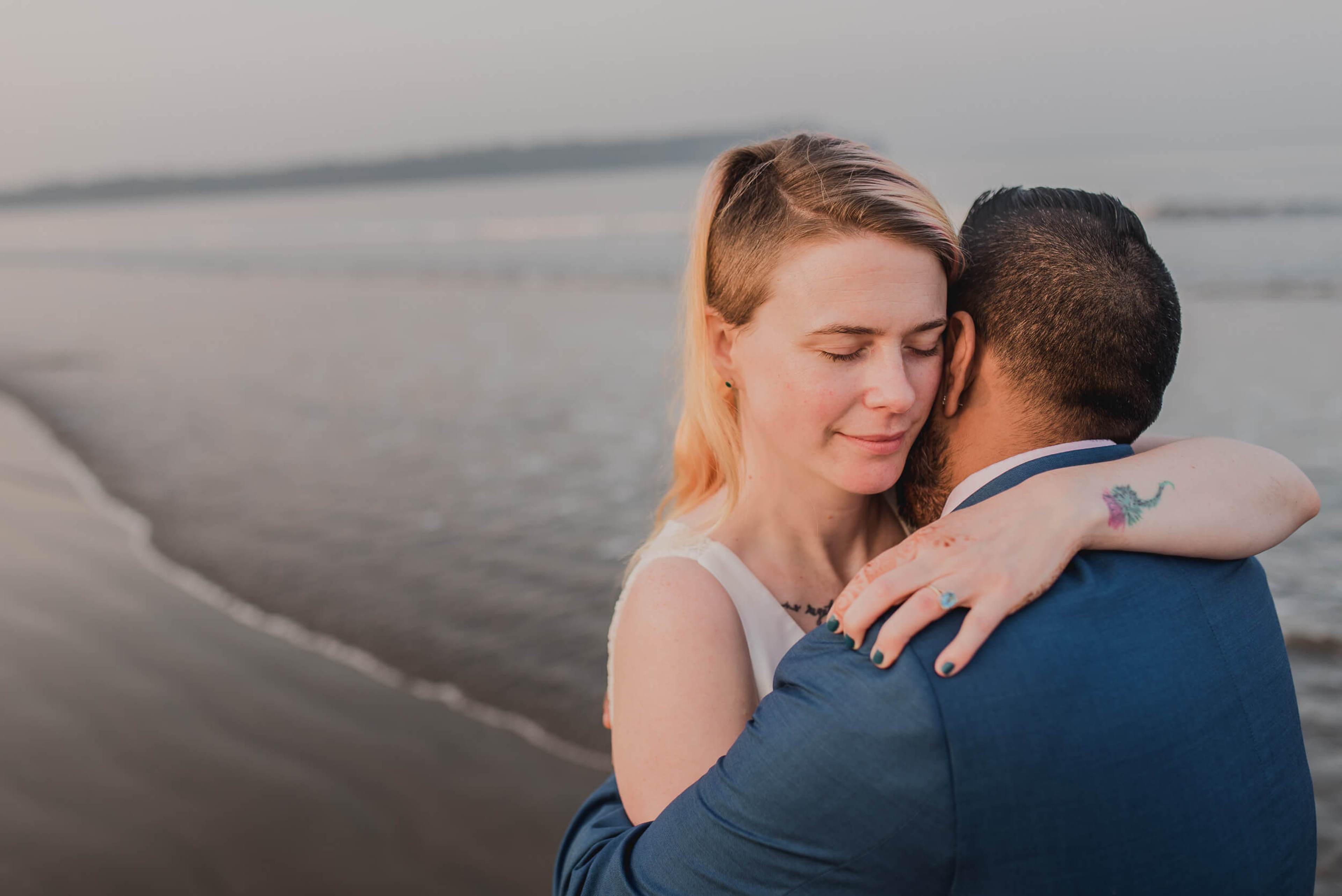 Sarah and Ravin embrace by the water at sunset in Goa, golden light on their faces