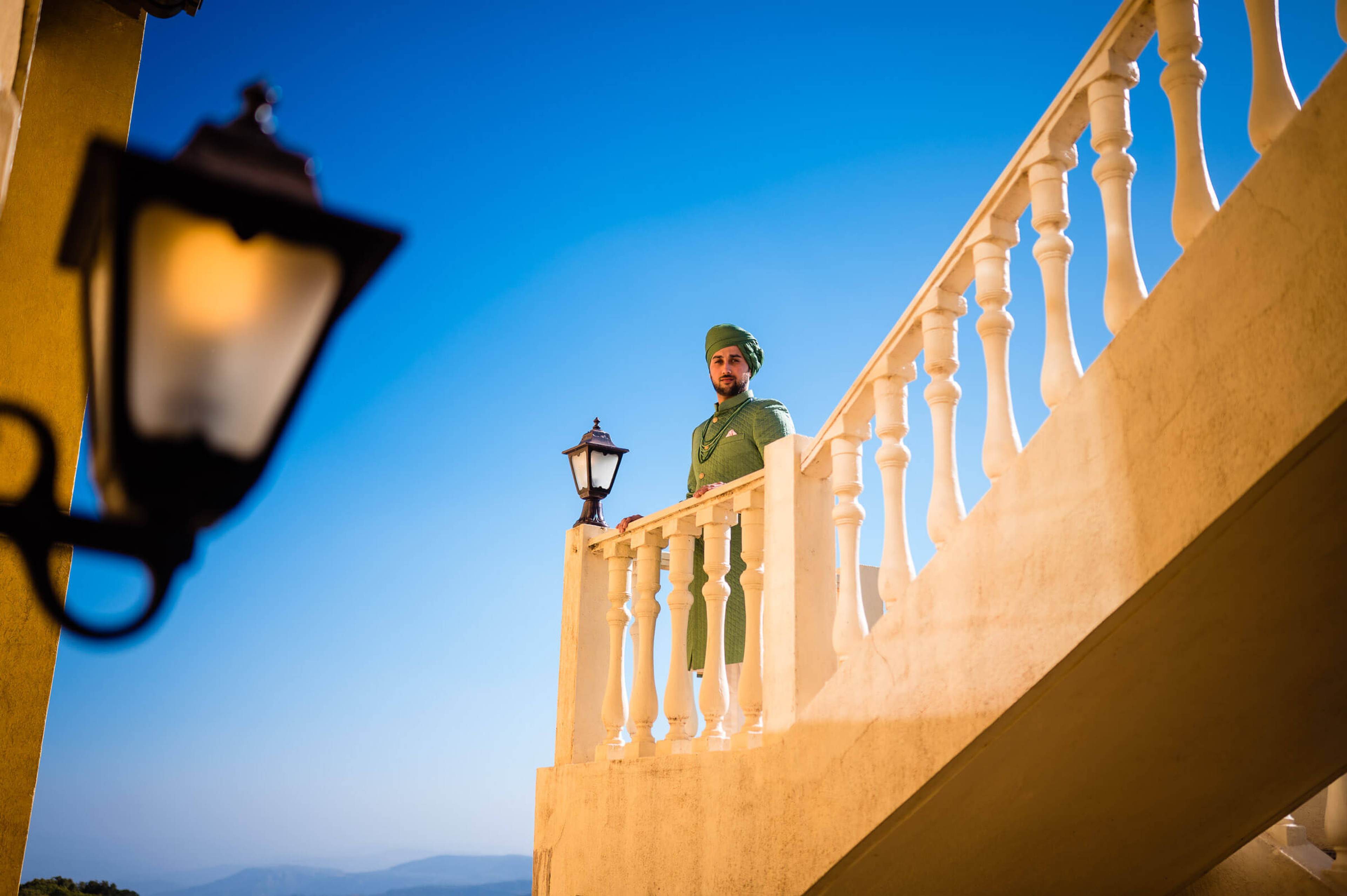 Yash stands on a terracotta balcony at dusk in Mahabaleshwar, clear blue sky behind