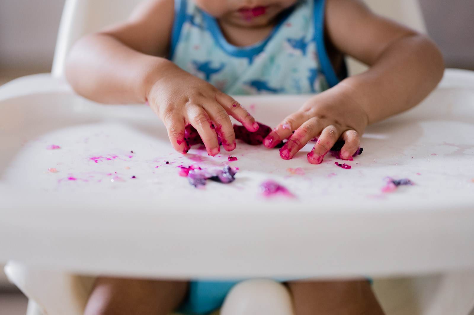 Young child in blue tie-dye shirt playing with pink and purple confetti on white table