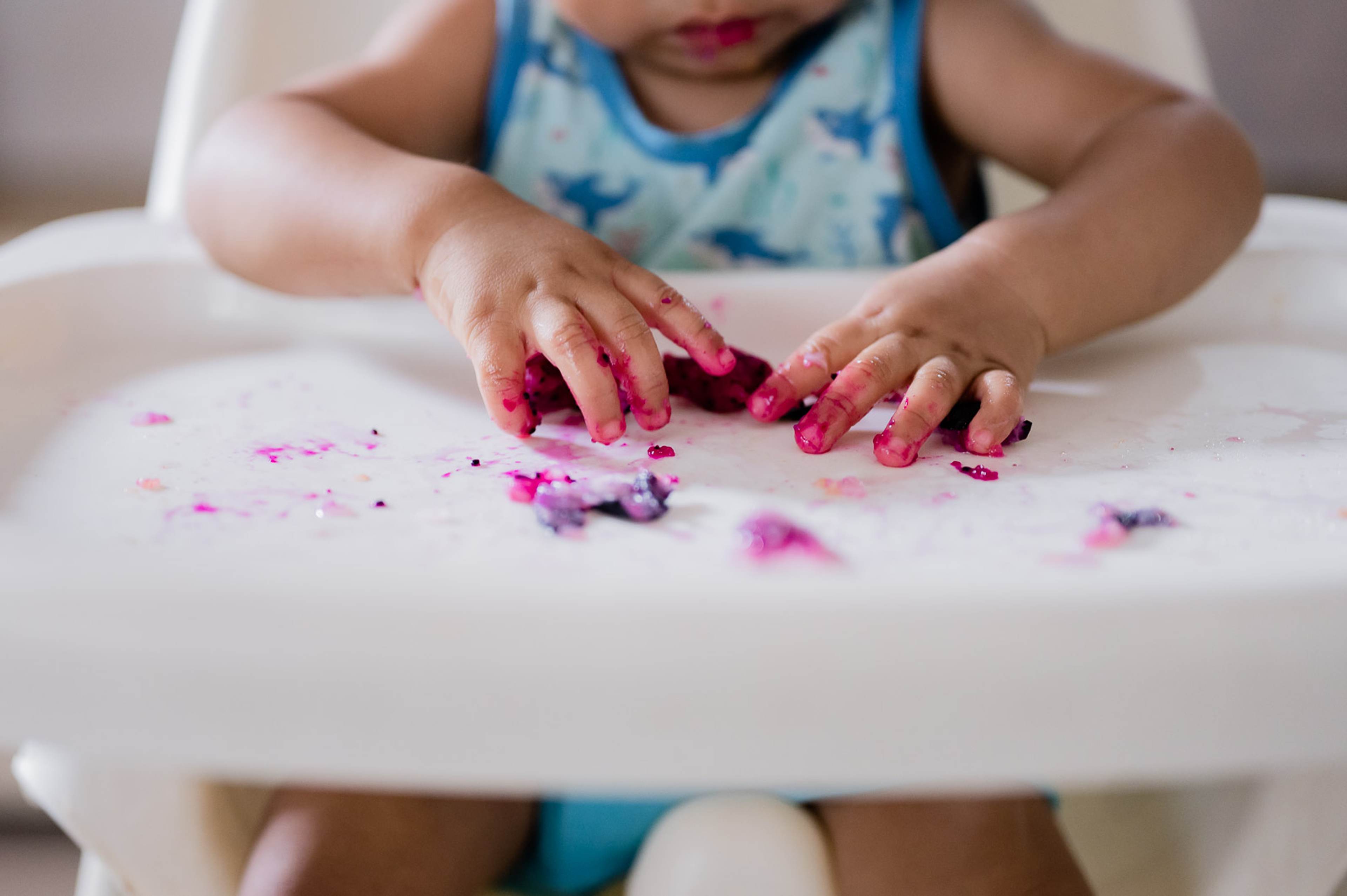 Young child in blue tie-dye shirt playing with pink and purple confetti on white table