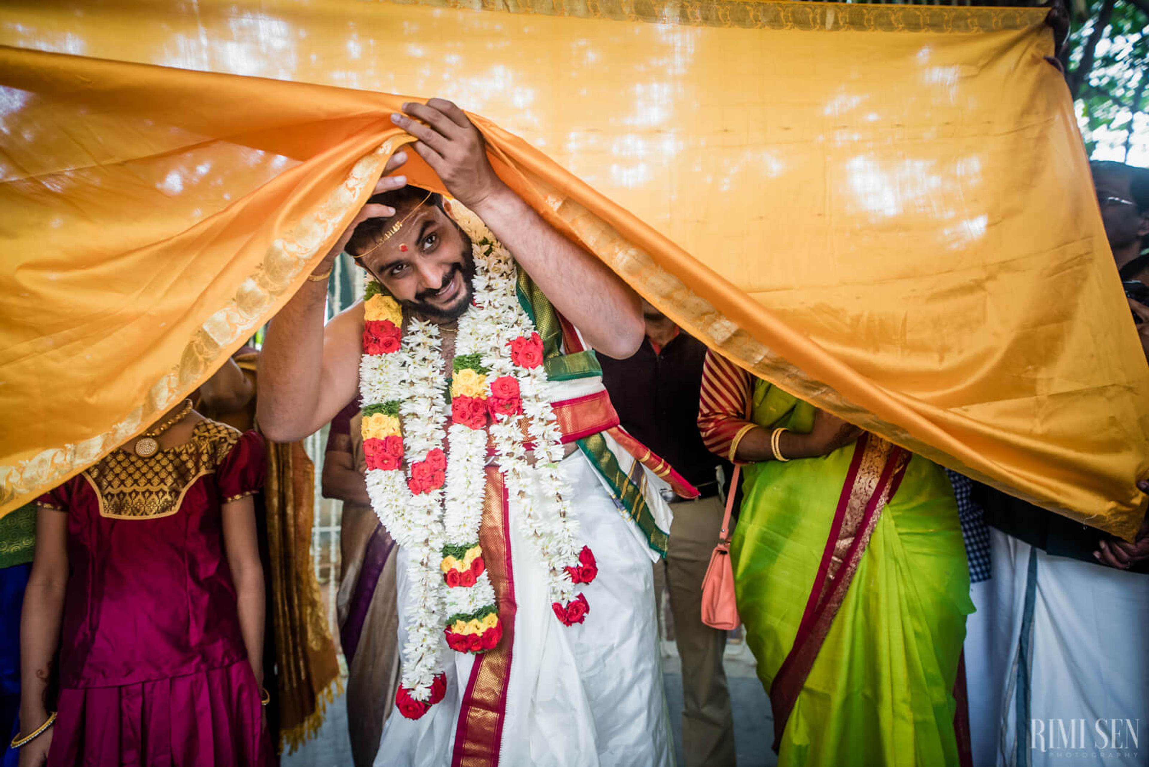 Groom Sridhar under golden canopy with floral garland, family members beside him in traditional attire