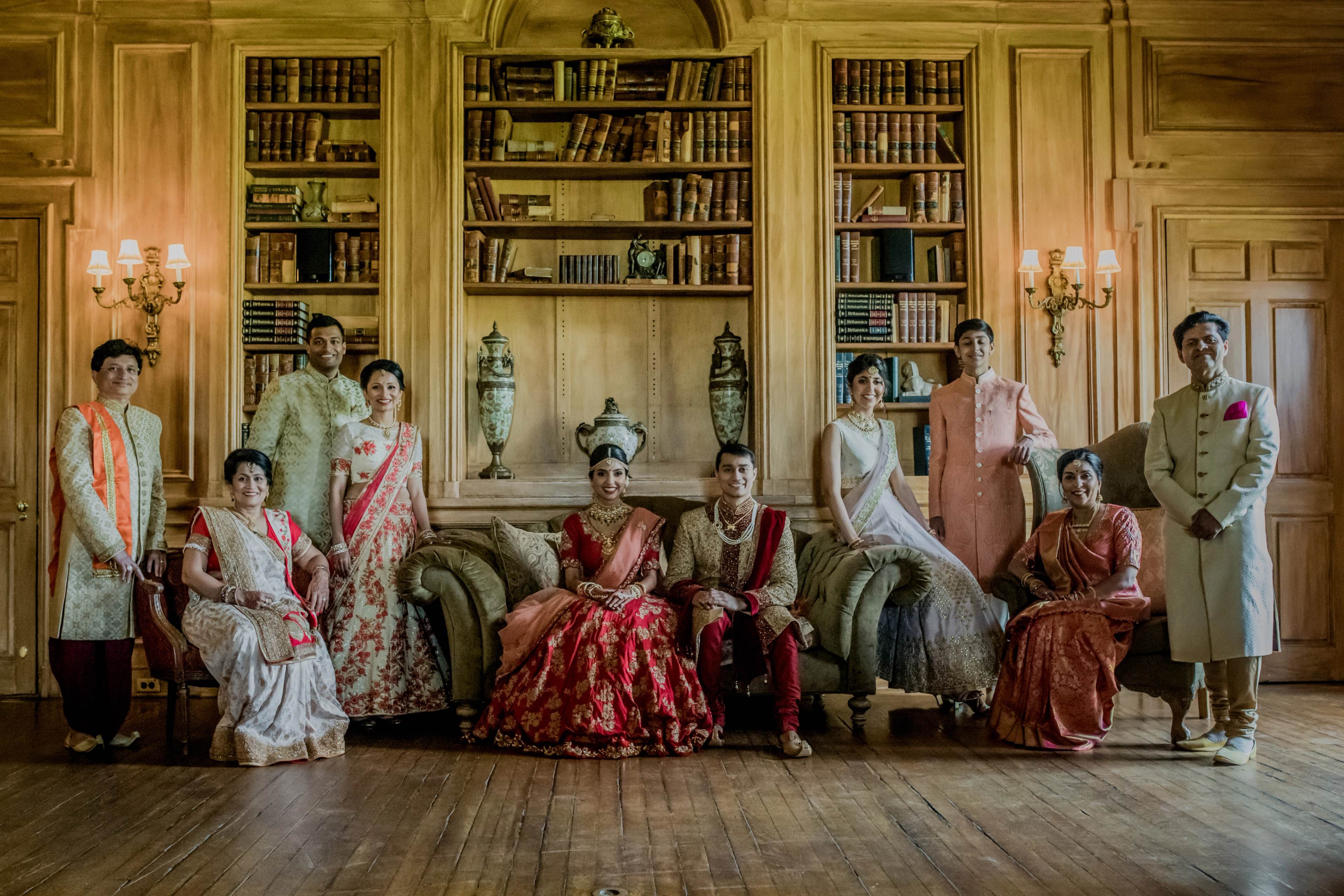Large family group in traditional South Asian attire posed in elegant library room with bookshelves and brass sconces