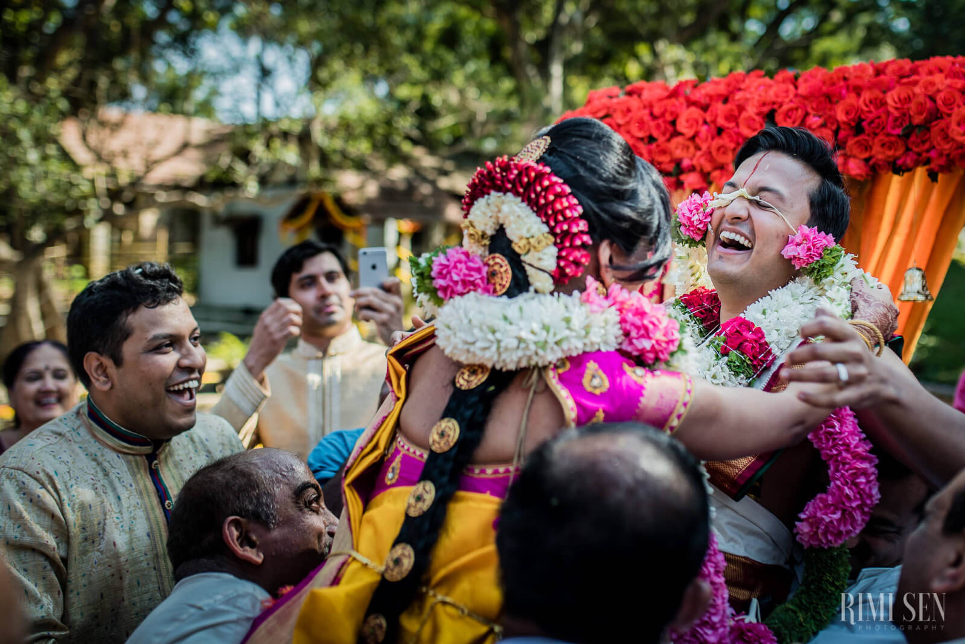 Pooja and Aniket celebrate with family and friends in vibrant traditional attire and pink and white flower garlands in Bangalore