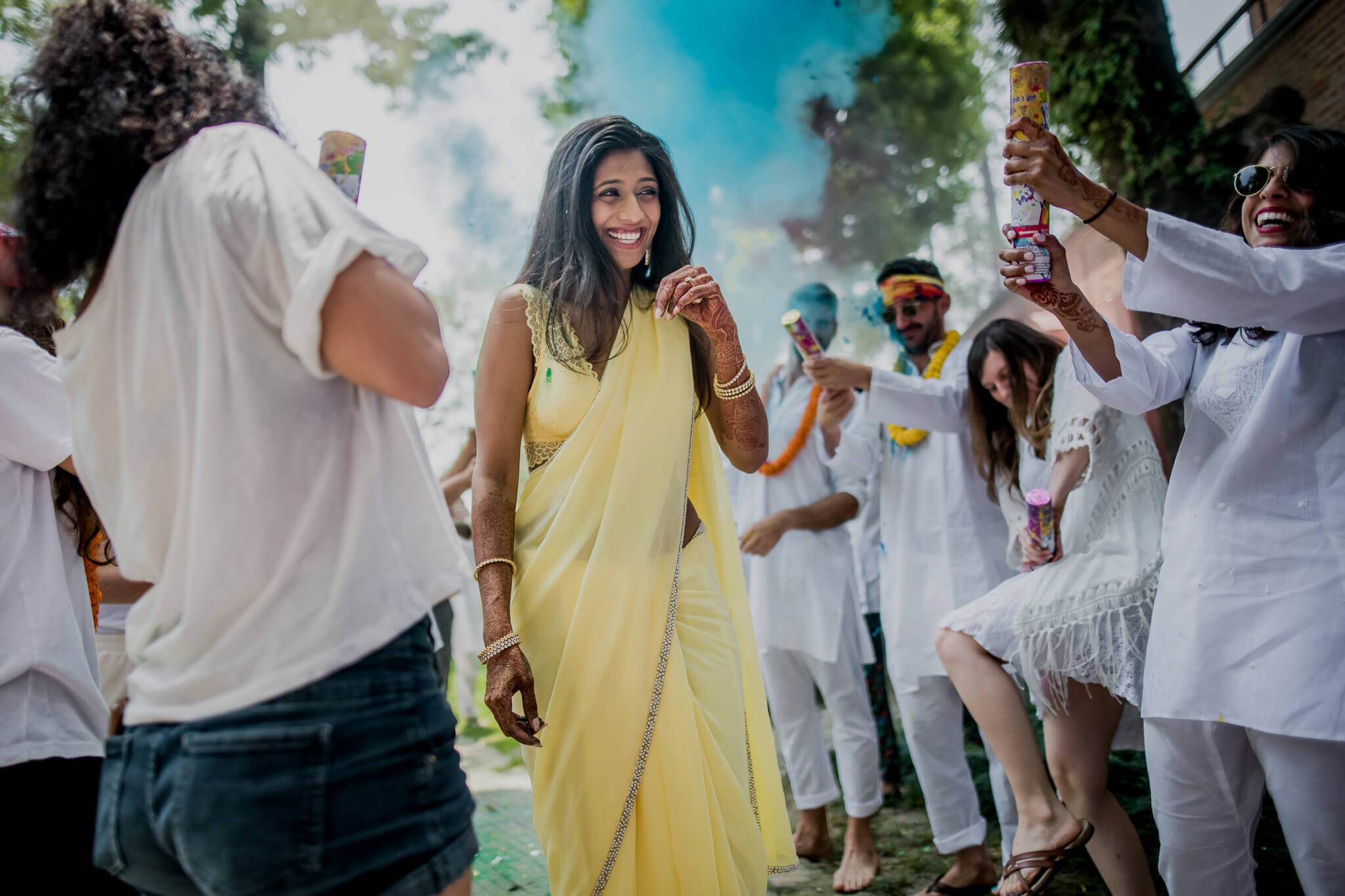Anu in yellow dress dancing with guests in white at sunny Nepal celebration