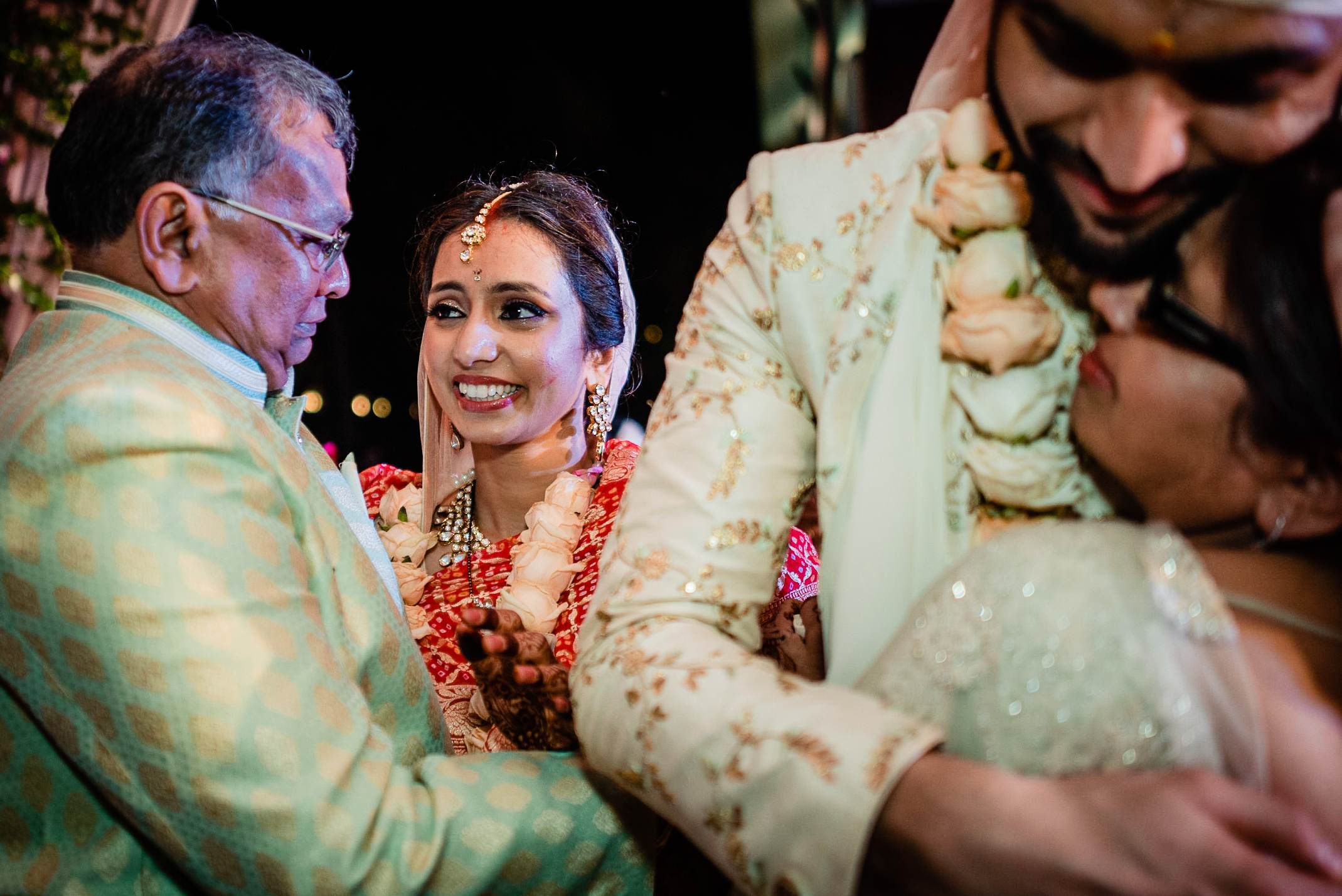 Avani smiles warmly while surrounded by family at her wedding ceremony in Goa, wearing red floral garland