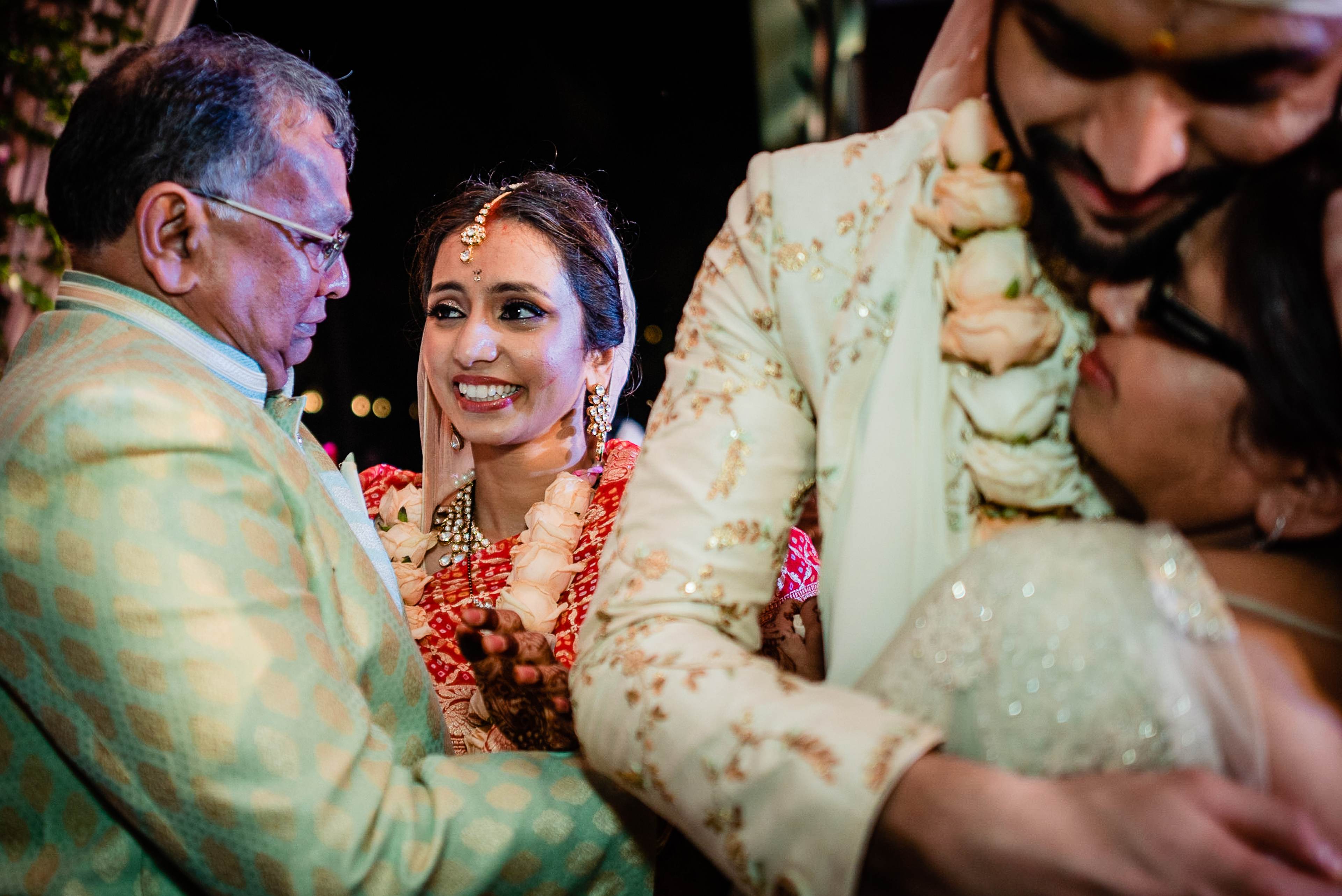 Avani smiles warmly while surrounded by family at her wedding ceremony in Goa, wearing red floral garland