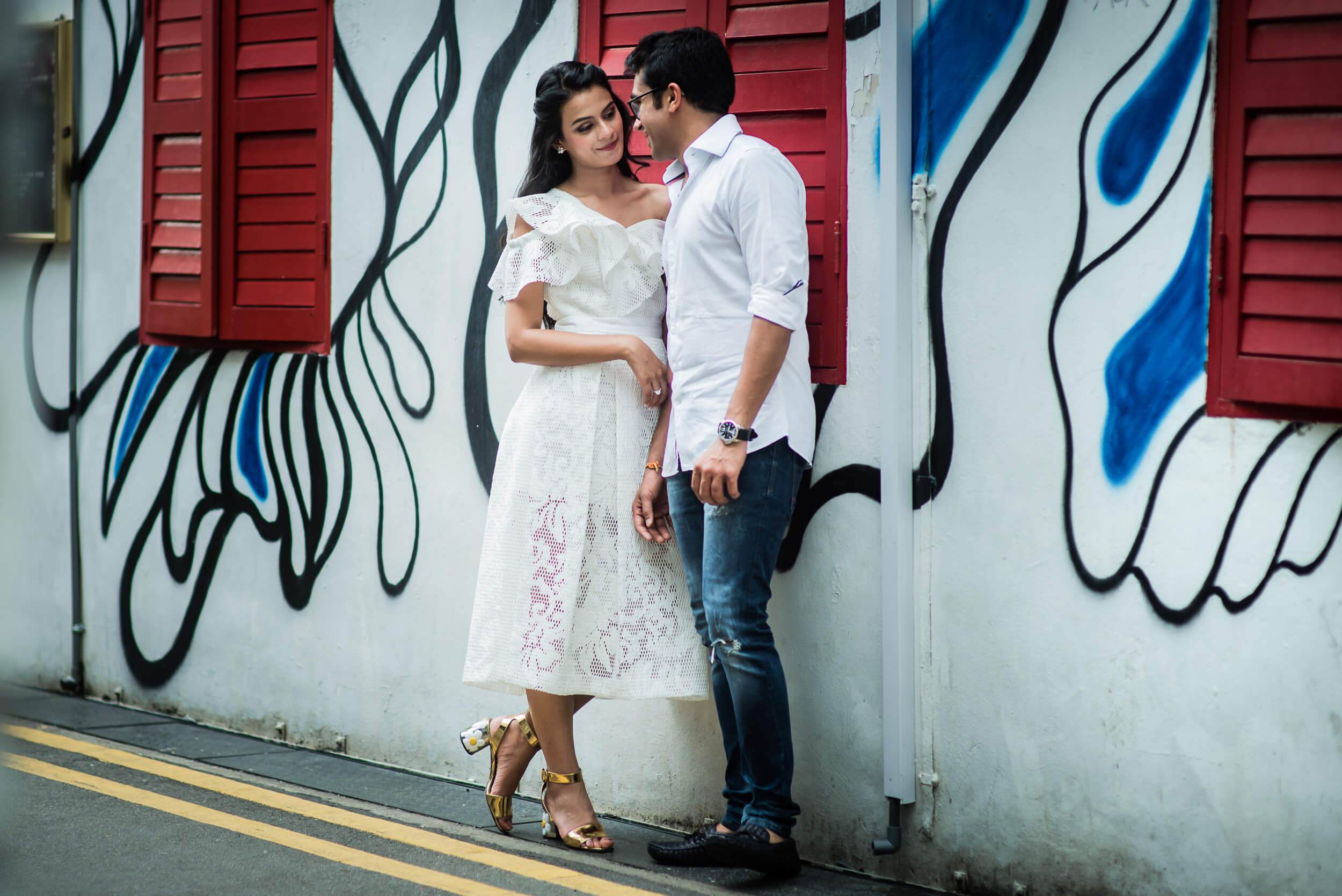 Yash and Disha embrace against vibrant street art with red shutters in Singapore