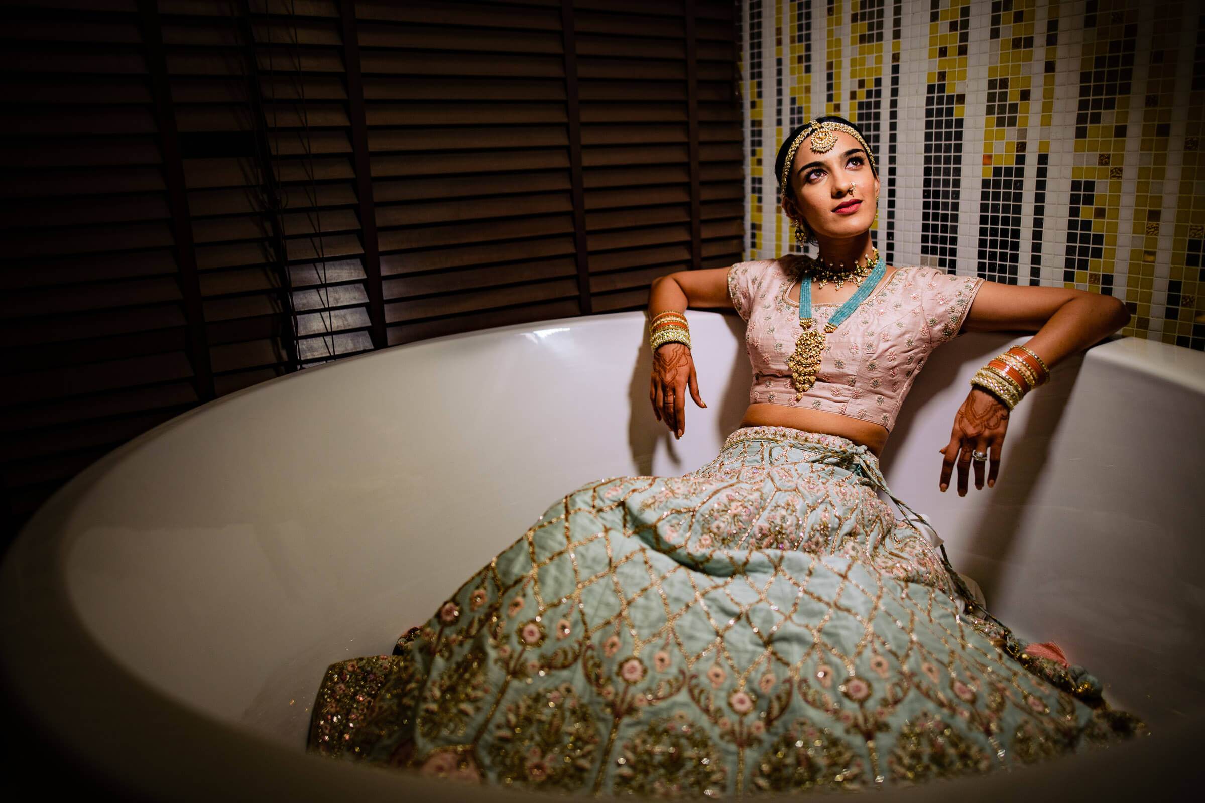 Shreya reclines in an ornate bathtub wearing an embellished cream and turquoise lehenga with gold jewelry