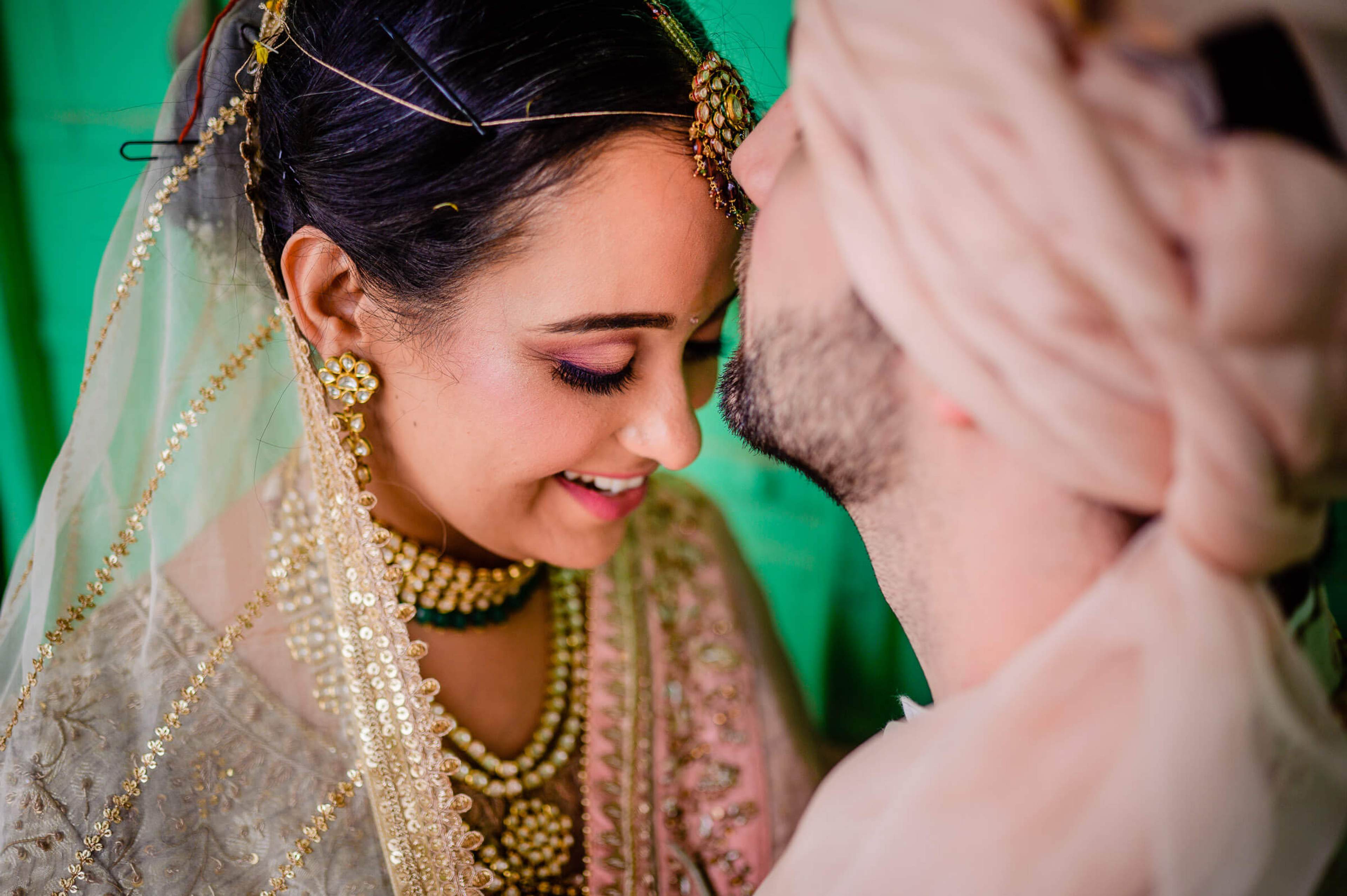 Maitrayee in embellished veil and gold jewelry smiles at Eric against green backdrop in Rajasthan