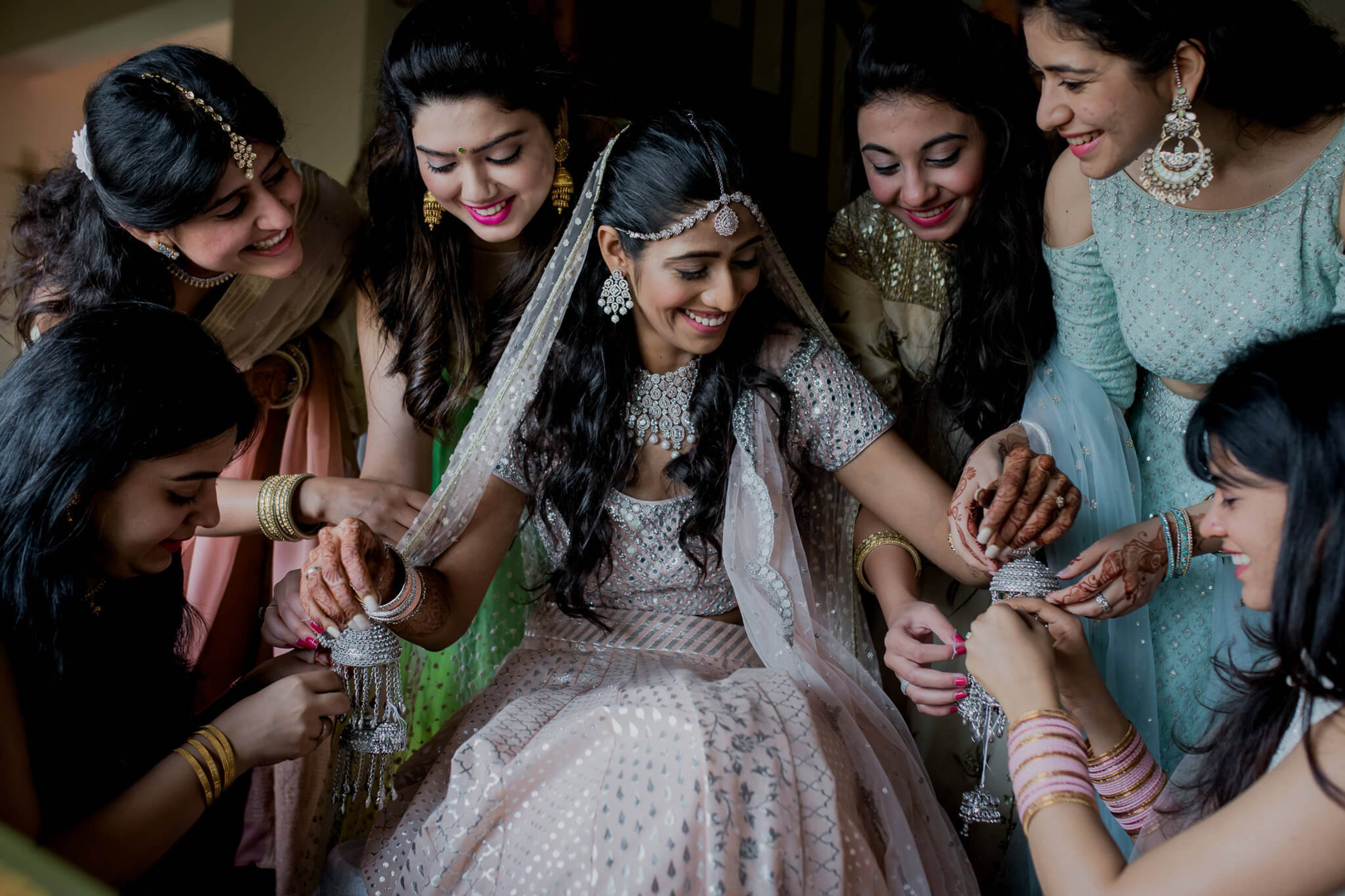 Anu surrounded by smiling women in traditional attire, adjusting her ornate bridal jewelry and veil