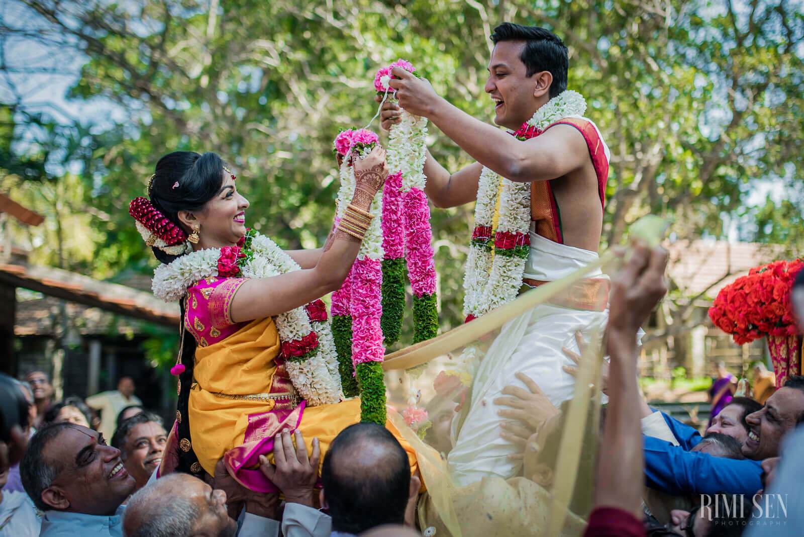 Pooja and Aniket exchange flower garlands during their Bangalore wedding ceremony, surrounded by smiling guests and vibrant blooms