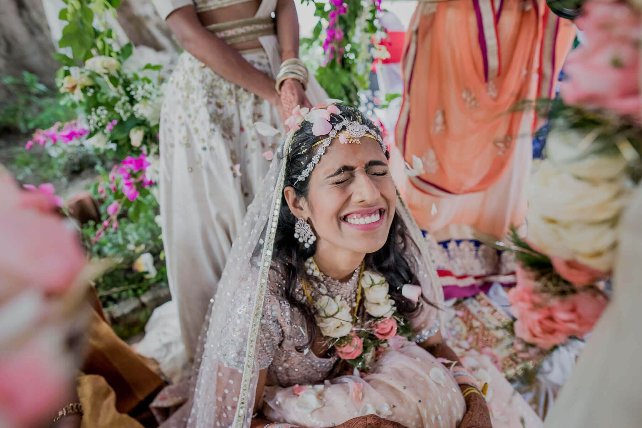 Anu smiles in embroidered wedding attire surrounded by pink flowers and greenery in Nepal