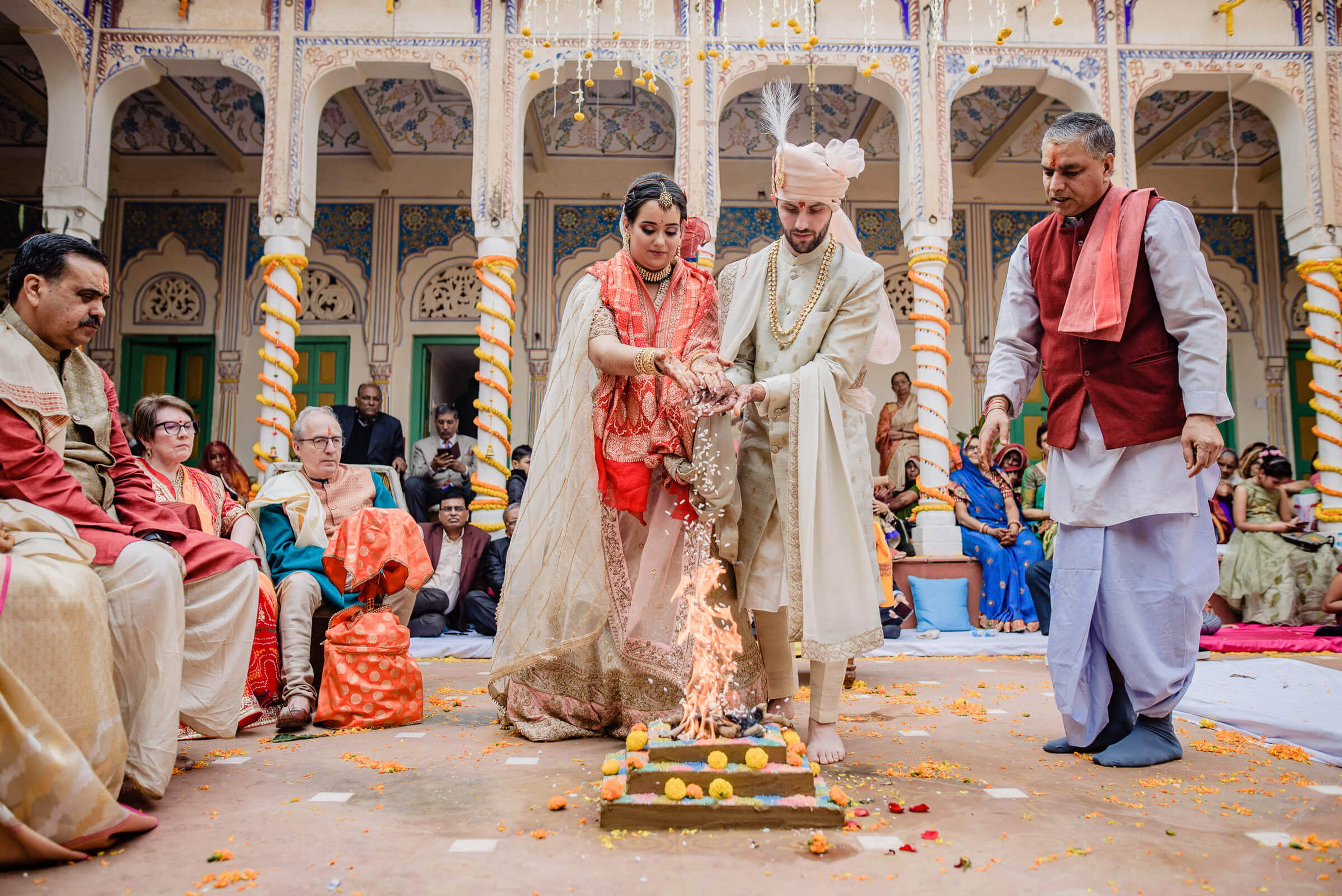 Maitrayee and Eric perform a ceremonial ritual in traditional attire at an ornate Rajasthan courtyard