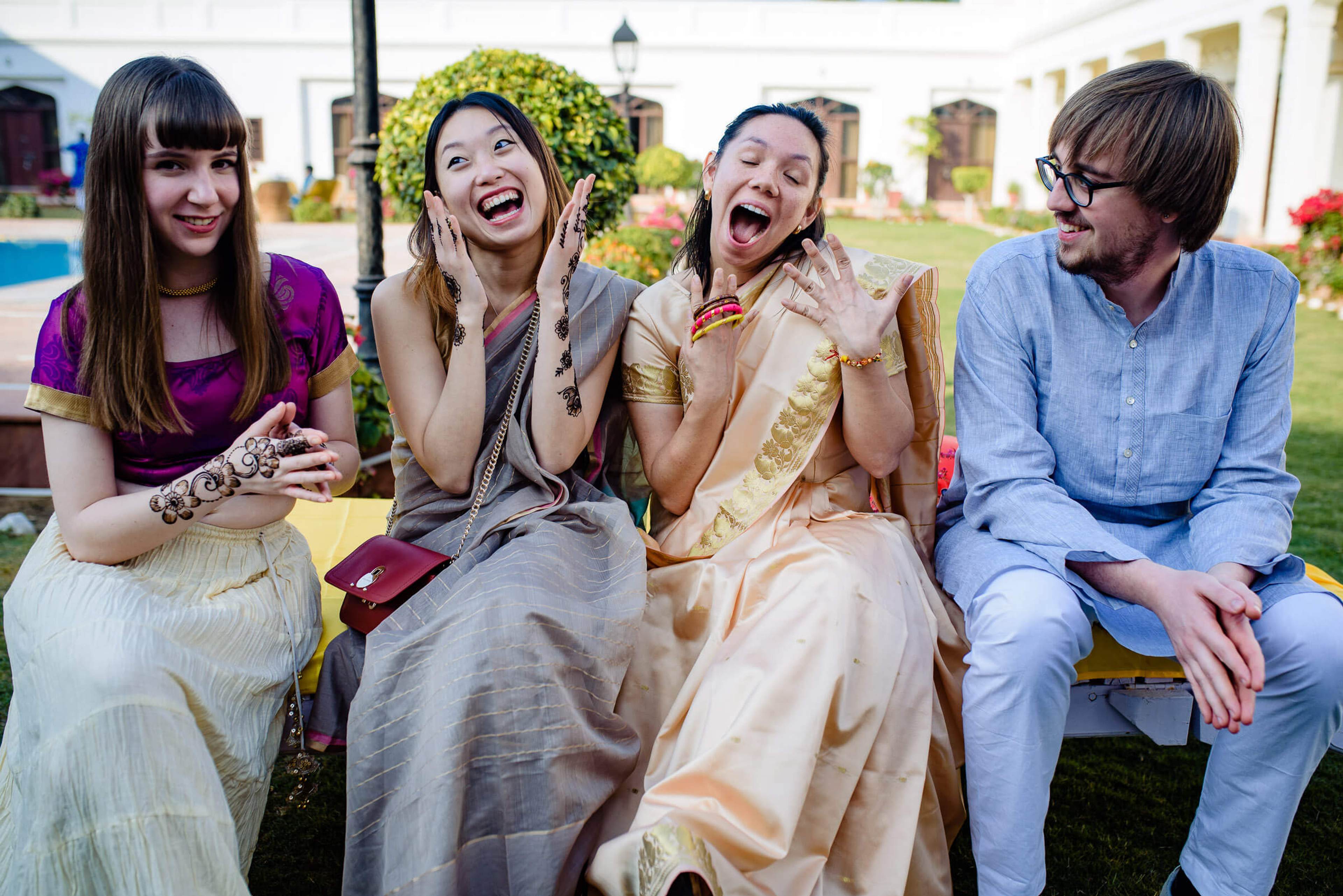 Four friends laugh together on a bench in a Rajasthan garden with colorful flowers