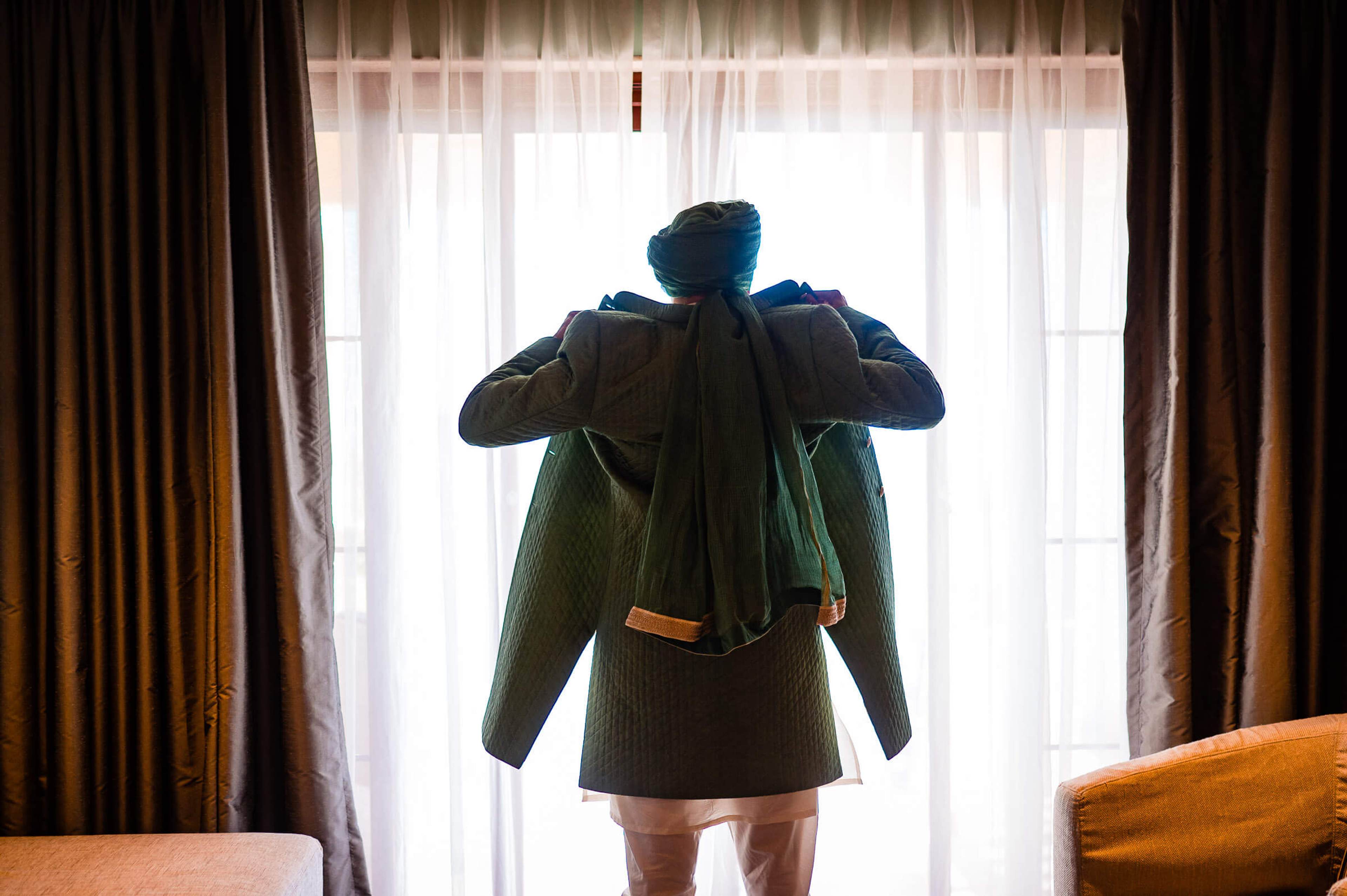 Shreya adjusting her blue jacket at a sunlit window, wearing olive-green dress, Mahabaleshwar