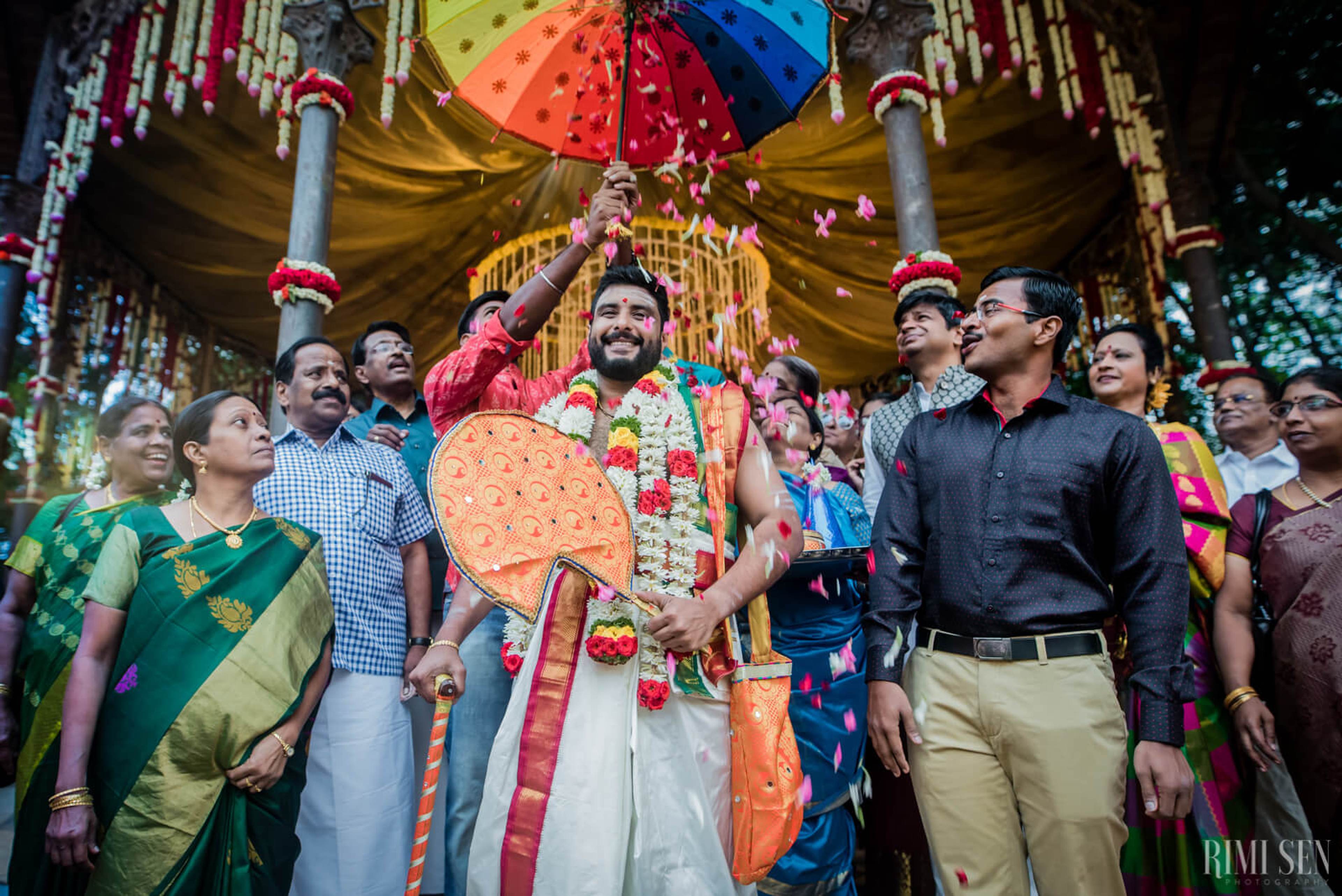 Groom Sridhar holds colorful umbrella amid festive crowd under ornate gold mandap at Bangalore wedding