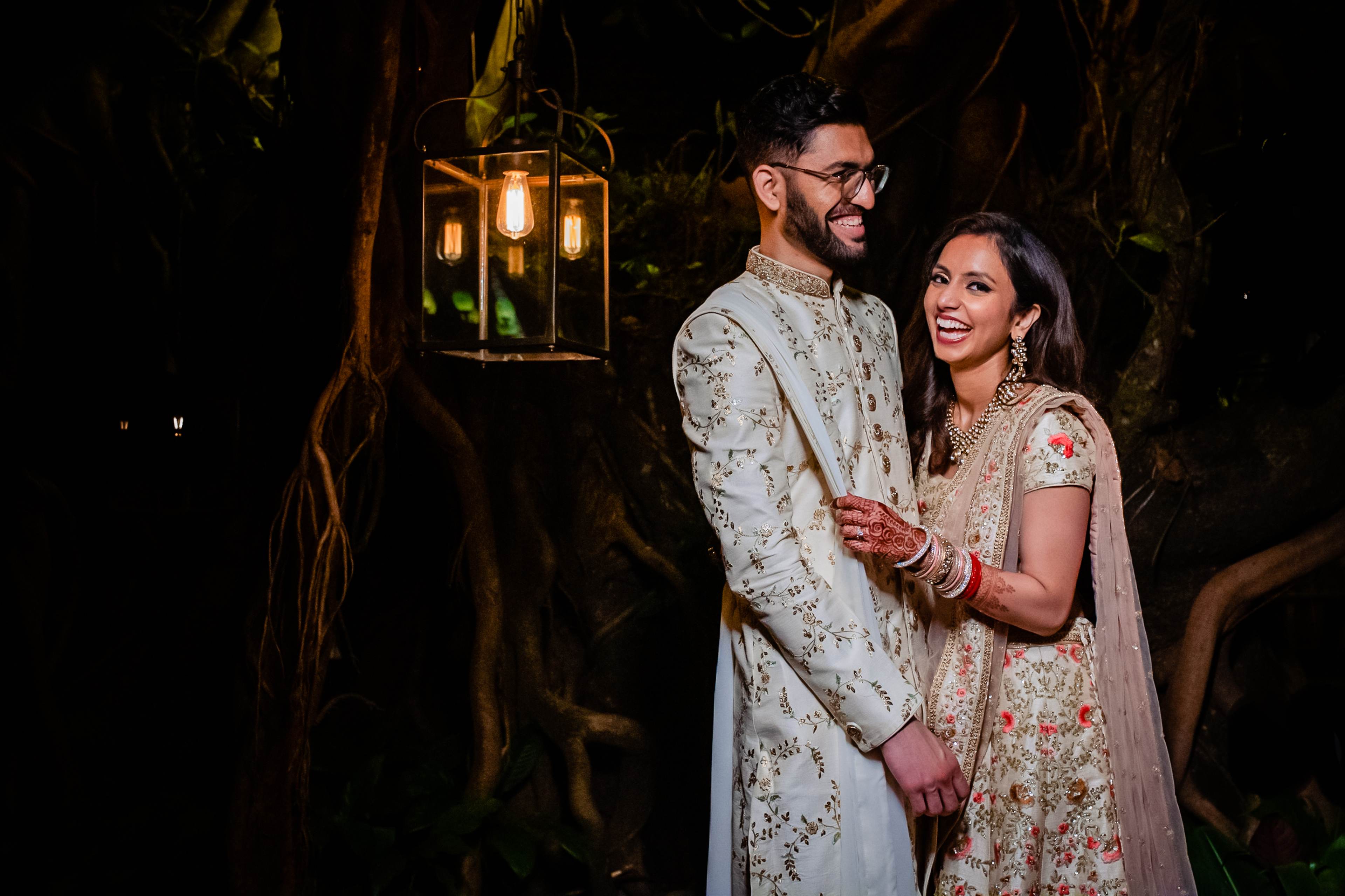 Avani and Srikant stand together in ornate traditional attire under glowing lanterns in Goa's nighttime setting
