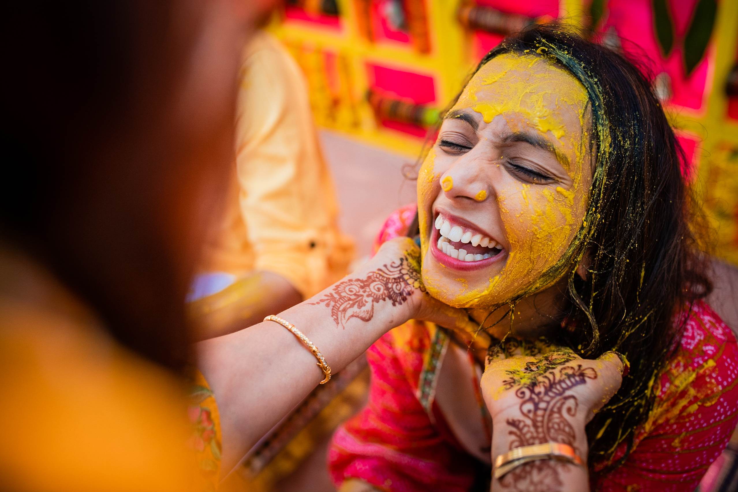 Avani laughs joyfully with yellow turmeric paste on her face, henna on her hands, wearing red during Haldi celebration in Goa