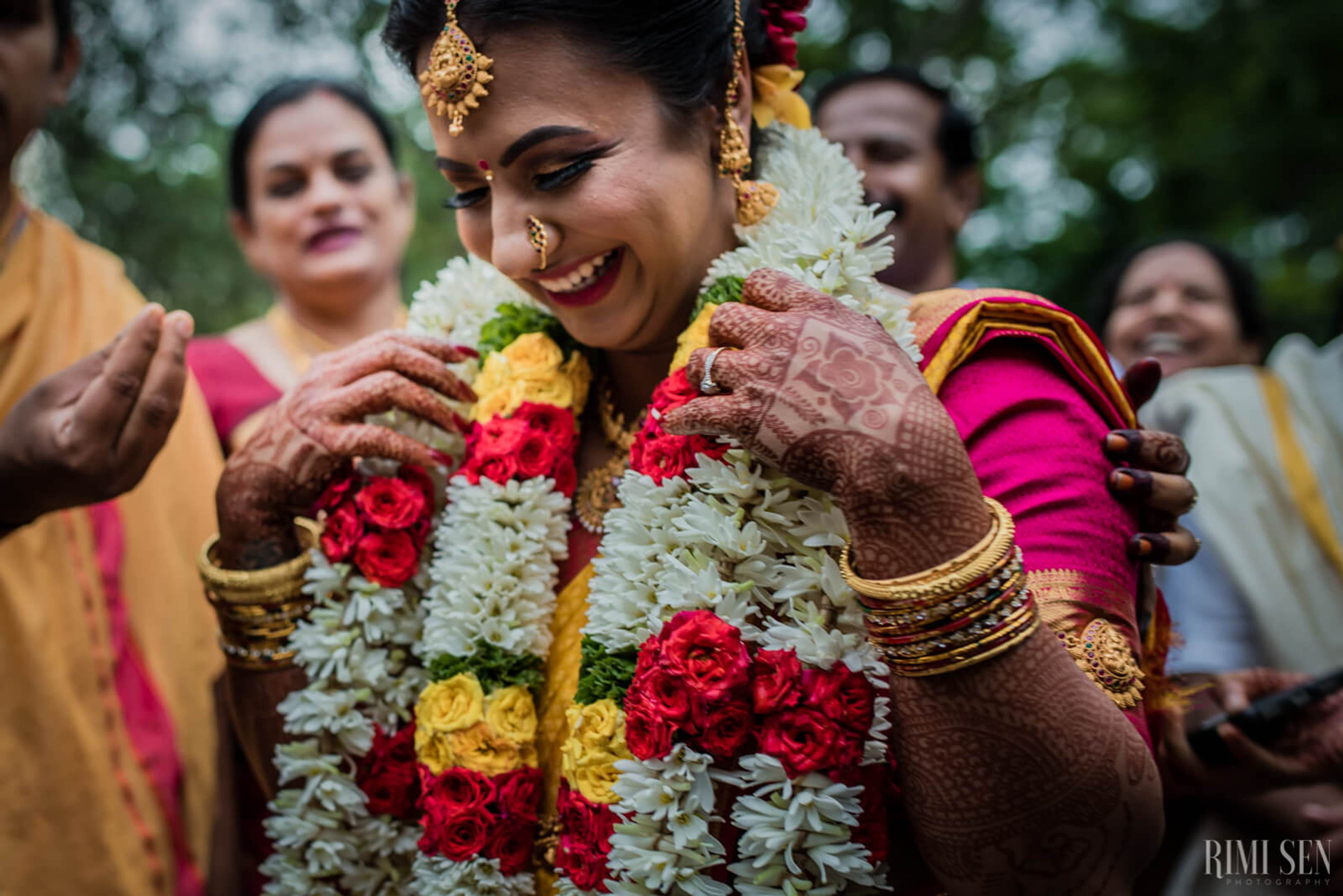 Nivetha smiling in vibrant pink silk, adorned with red and white flower garland at Bangalore wedding
