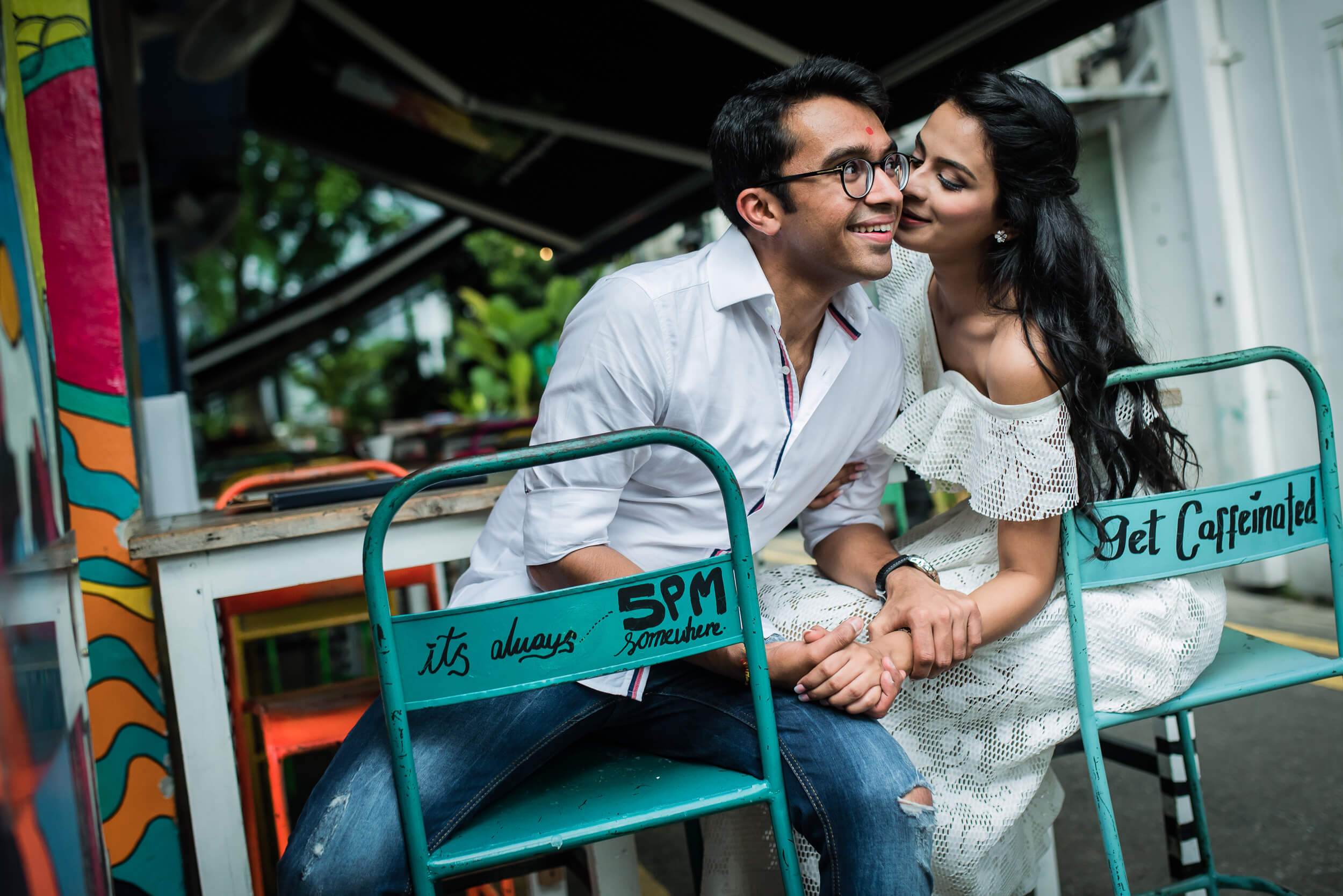Yash and Disha sit close on a colorful bench at a casual Singapore café, sharing an affectionate moment