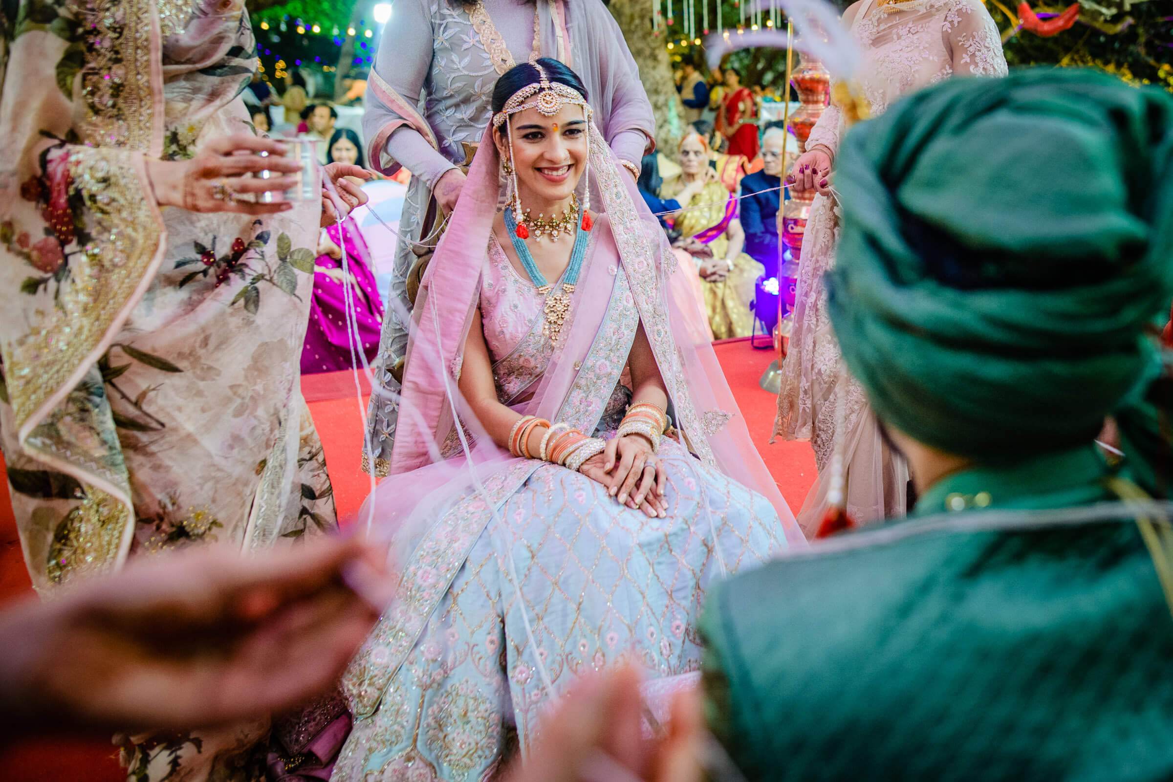 Shreya in pastel pink wedding lehenga smiles seated at Mahabaleshwar celebration surrounded by guests