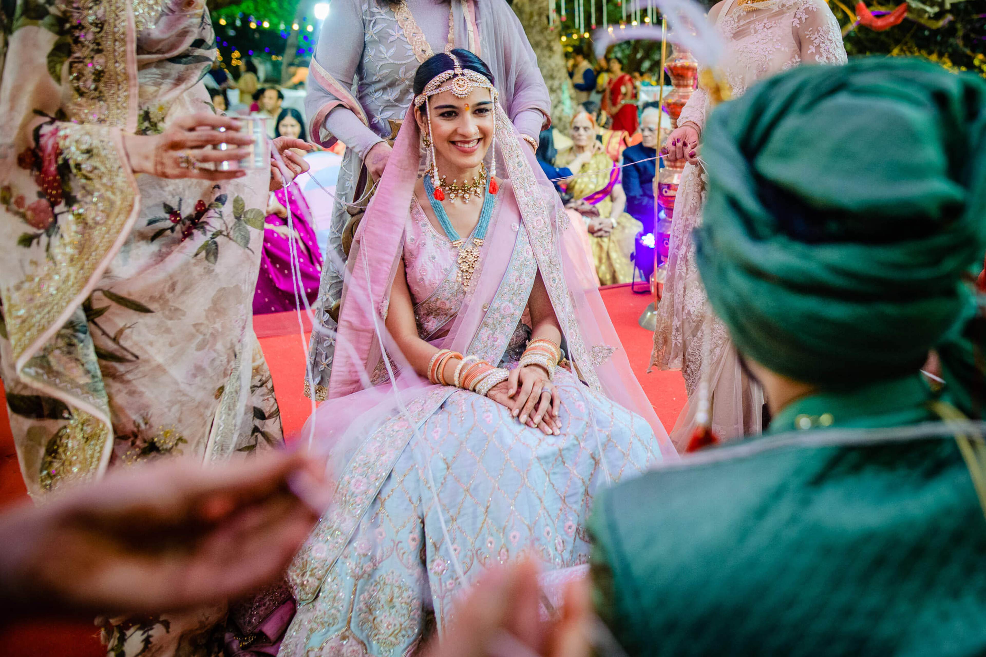 Shreya in pastel pink wedding lehenga smiles seated at Mahabaleshwar celebration surrounded by guests