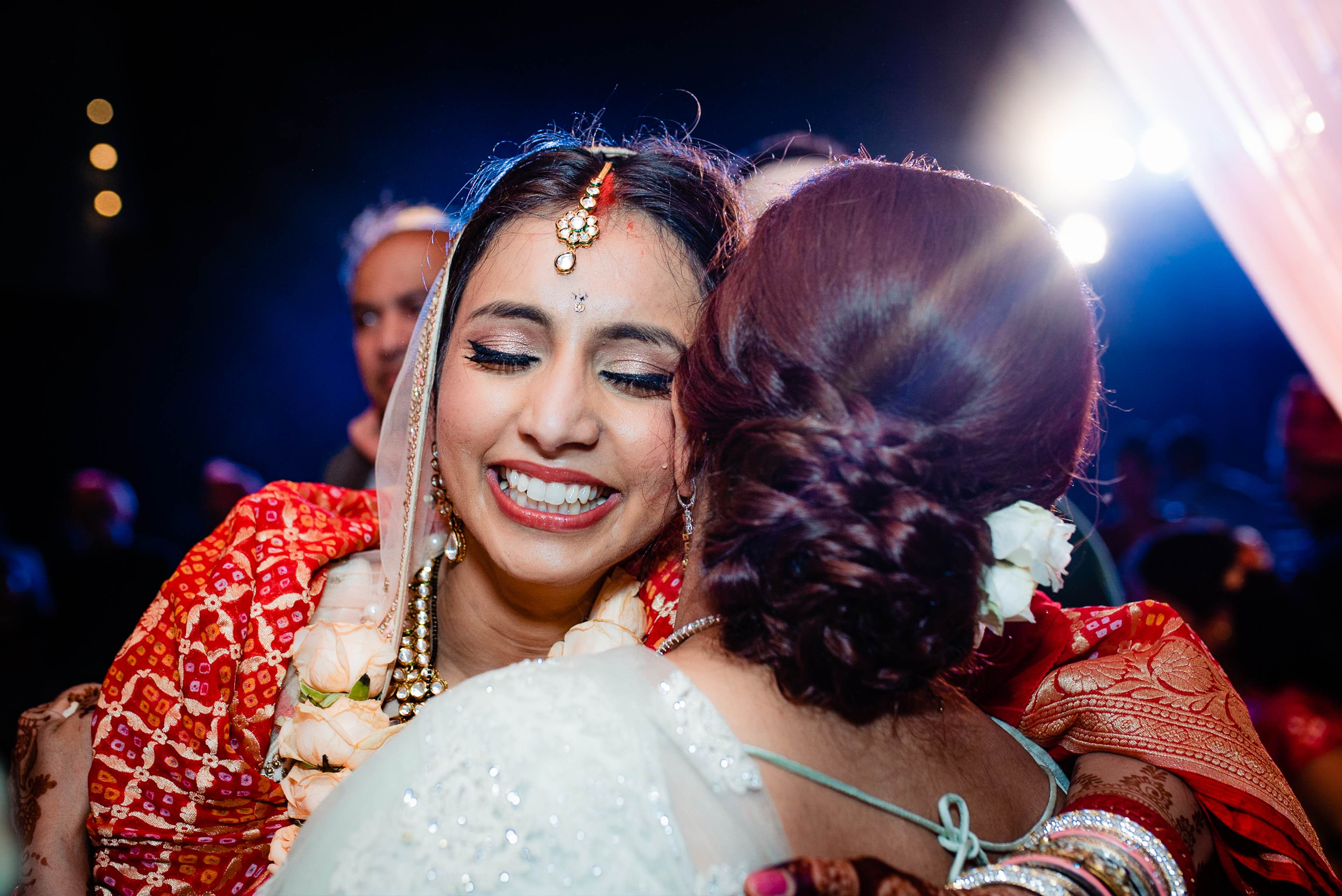 Avani in red embroidered lehenga embraces guest at Goa wedding celebration, dramatic blue stage lighting