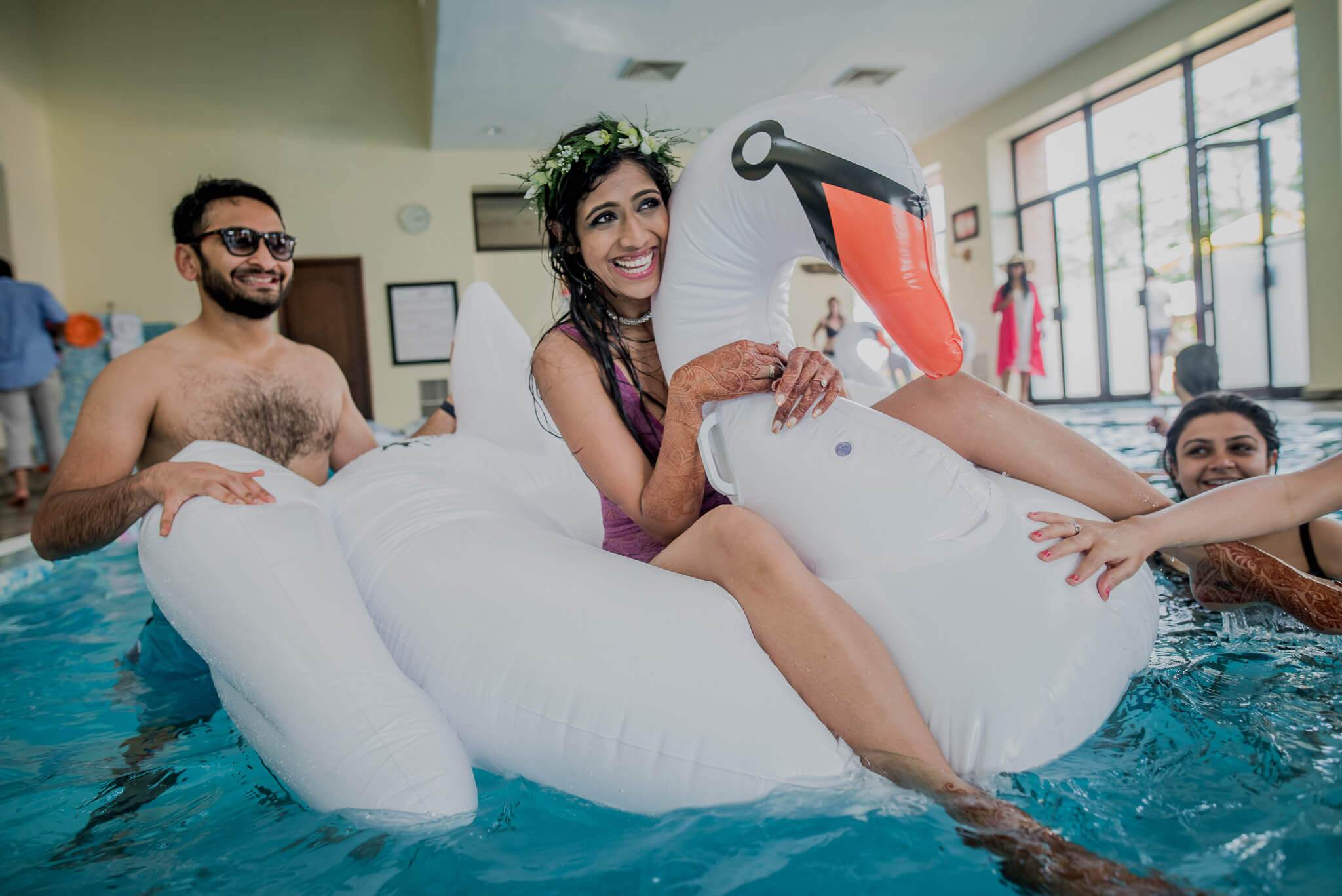 Anu and Raghu playfully float on inflatable pool toys in an indoor swimming pool with friends watching