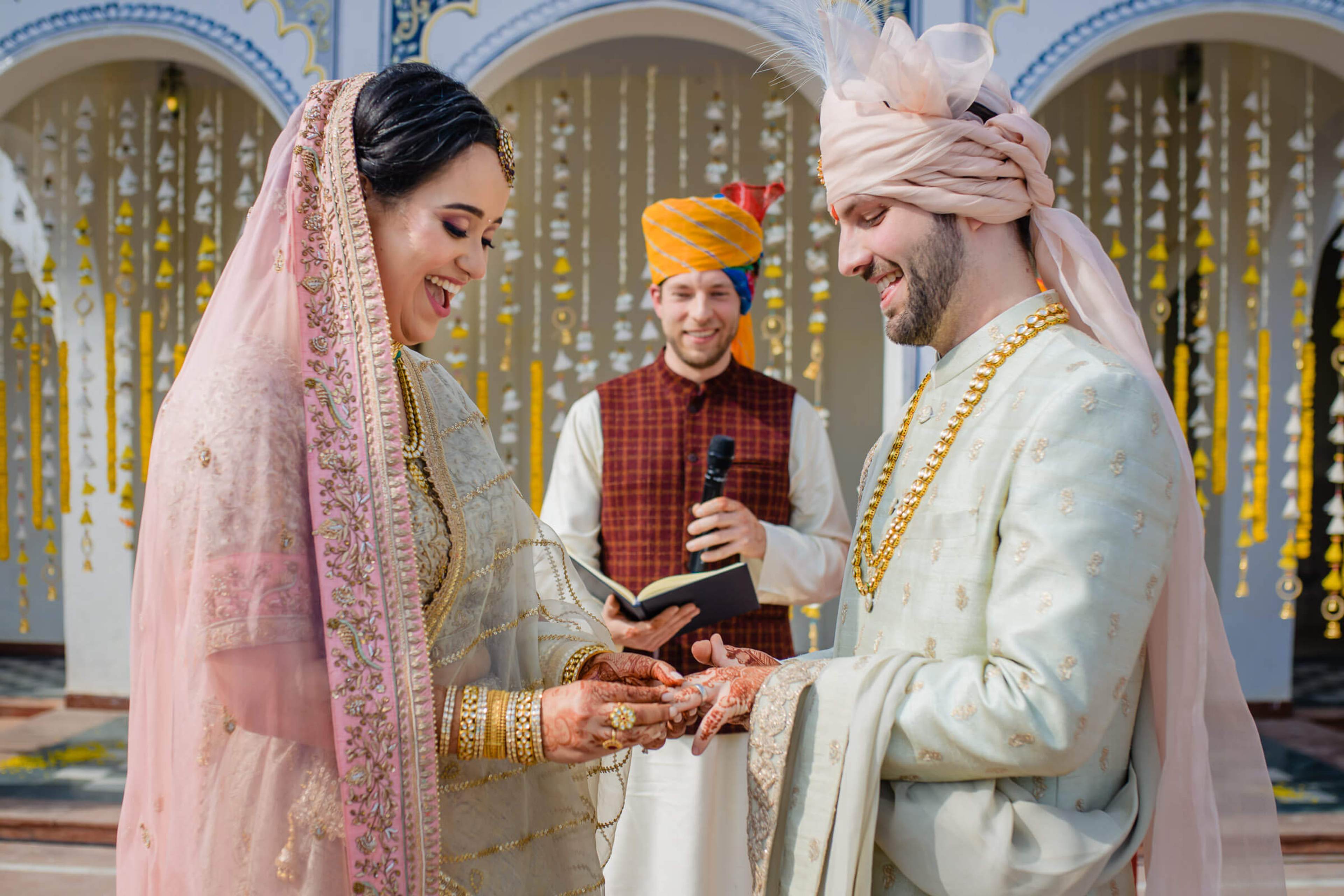 Maitrayee and Eric exchange rings during their wedding ceremony in Rajasthan, ornate blue doors behind them