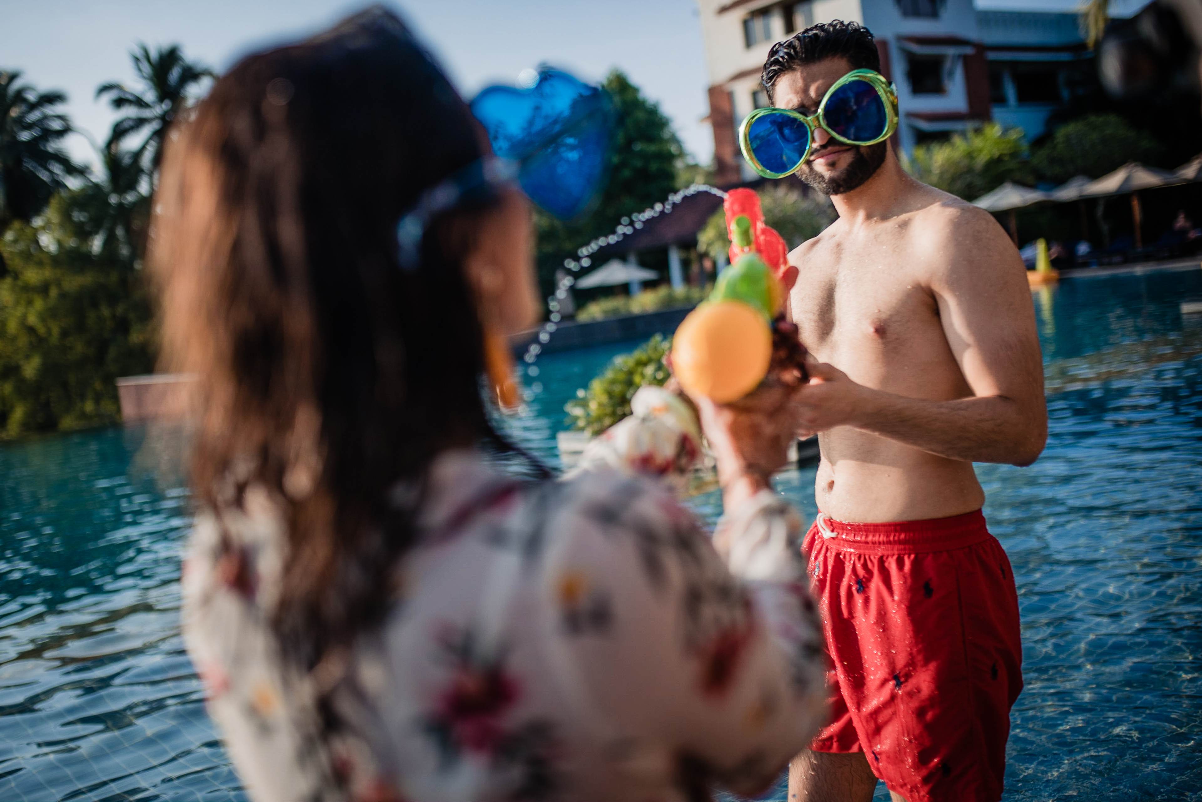 Avani and Srikant play with water balloons by the pool in Goa, laughing in summer sunlight