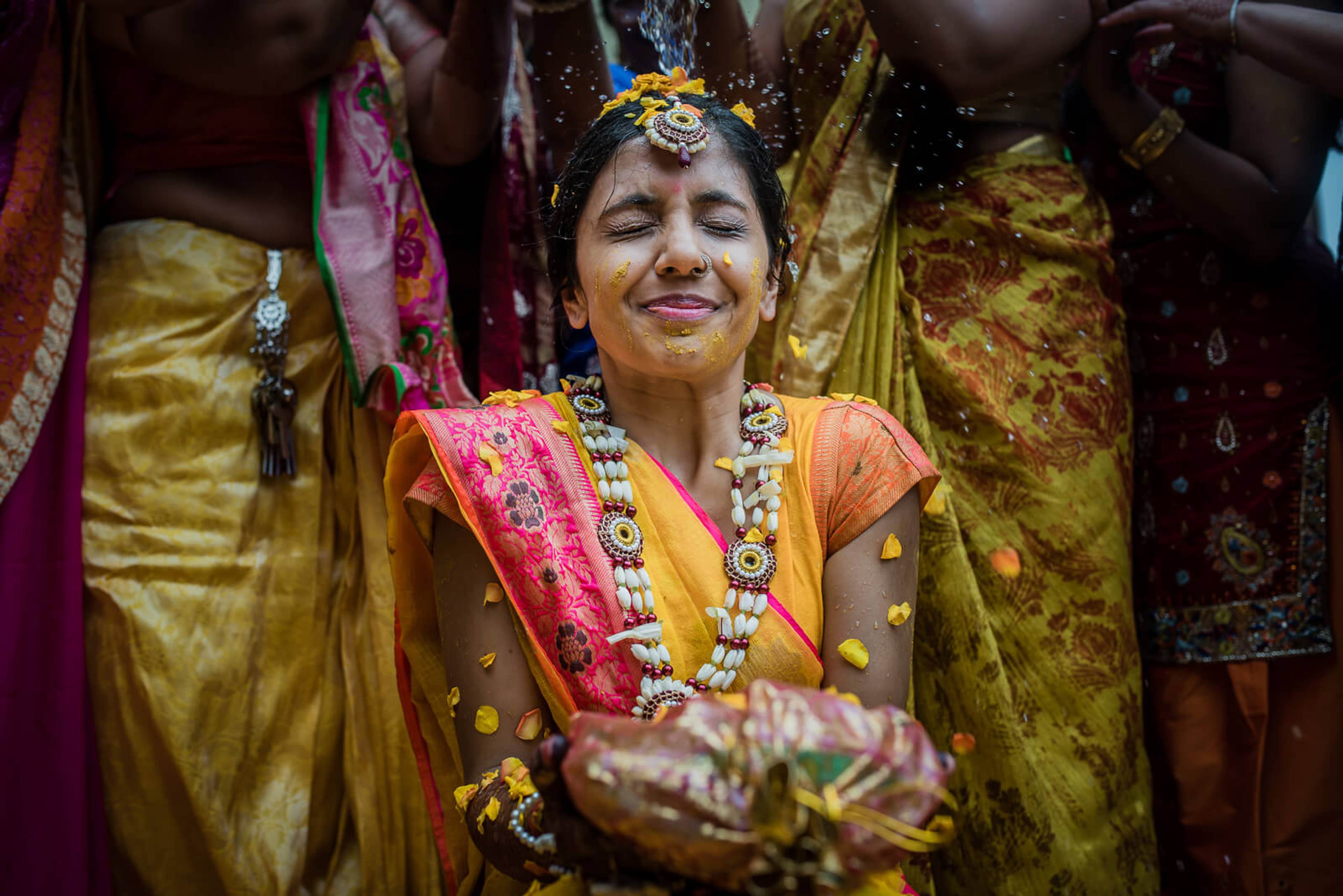 Barkha in traditional gold and coral silk attire with pearl jewelry, surrounded by draped fabrics at New York wedding