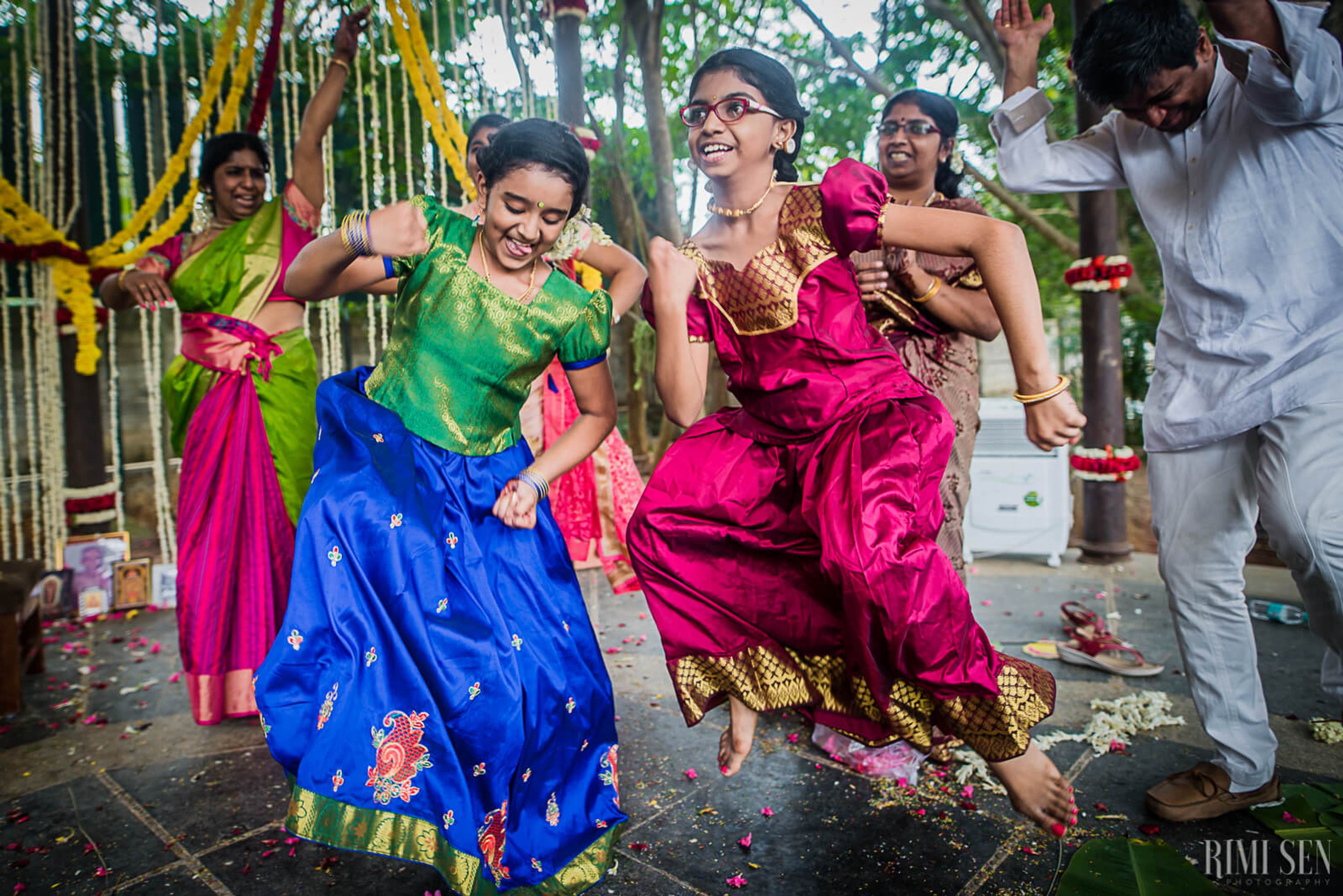 Guests dancing joyfully in vibrant traditional attire at Bangalore wedding celebration with decorated bamboo arch