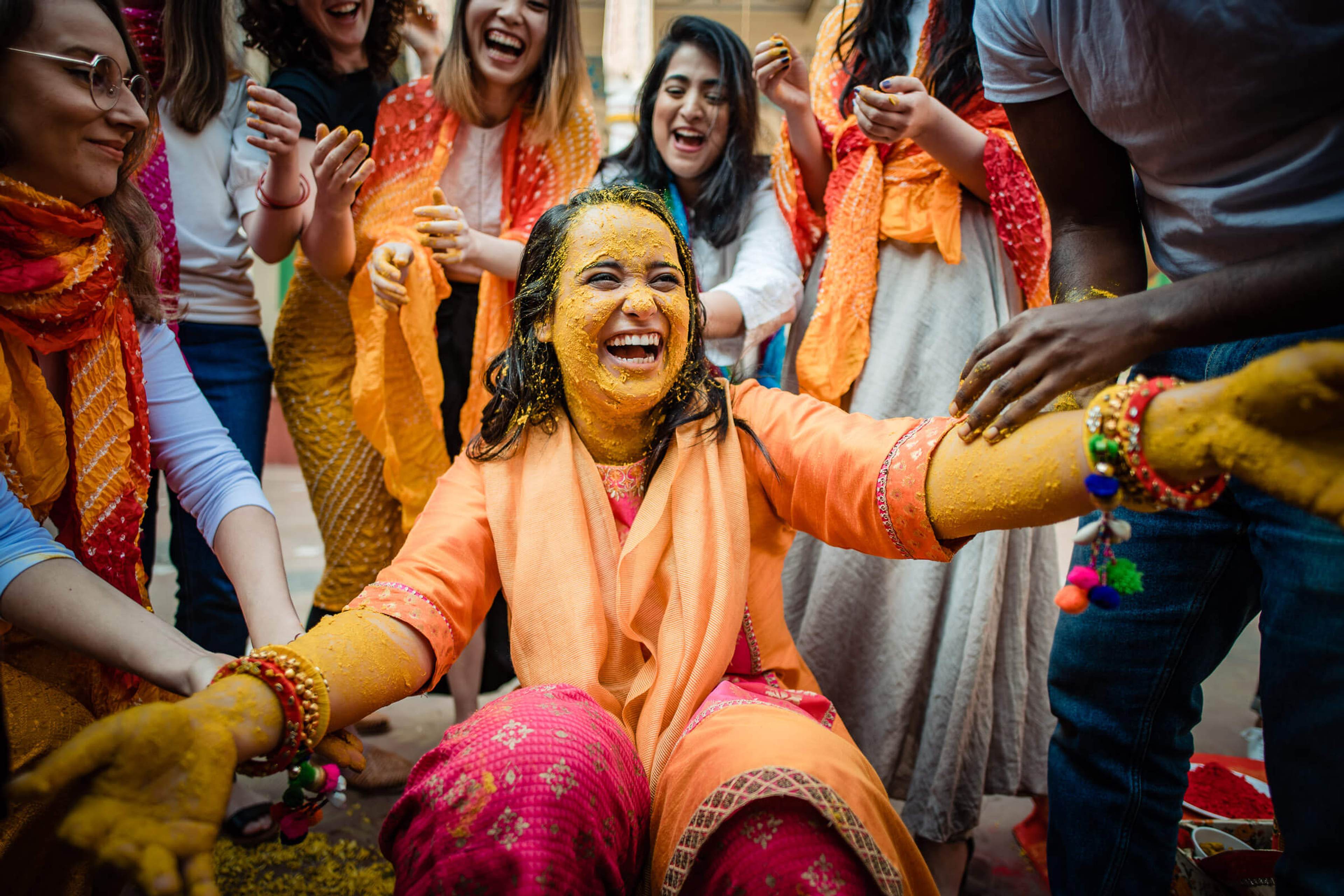 Maitrayee surrounded by joyful guests in vibrant orange and pink silks during Rajasthan celebration