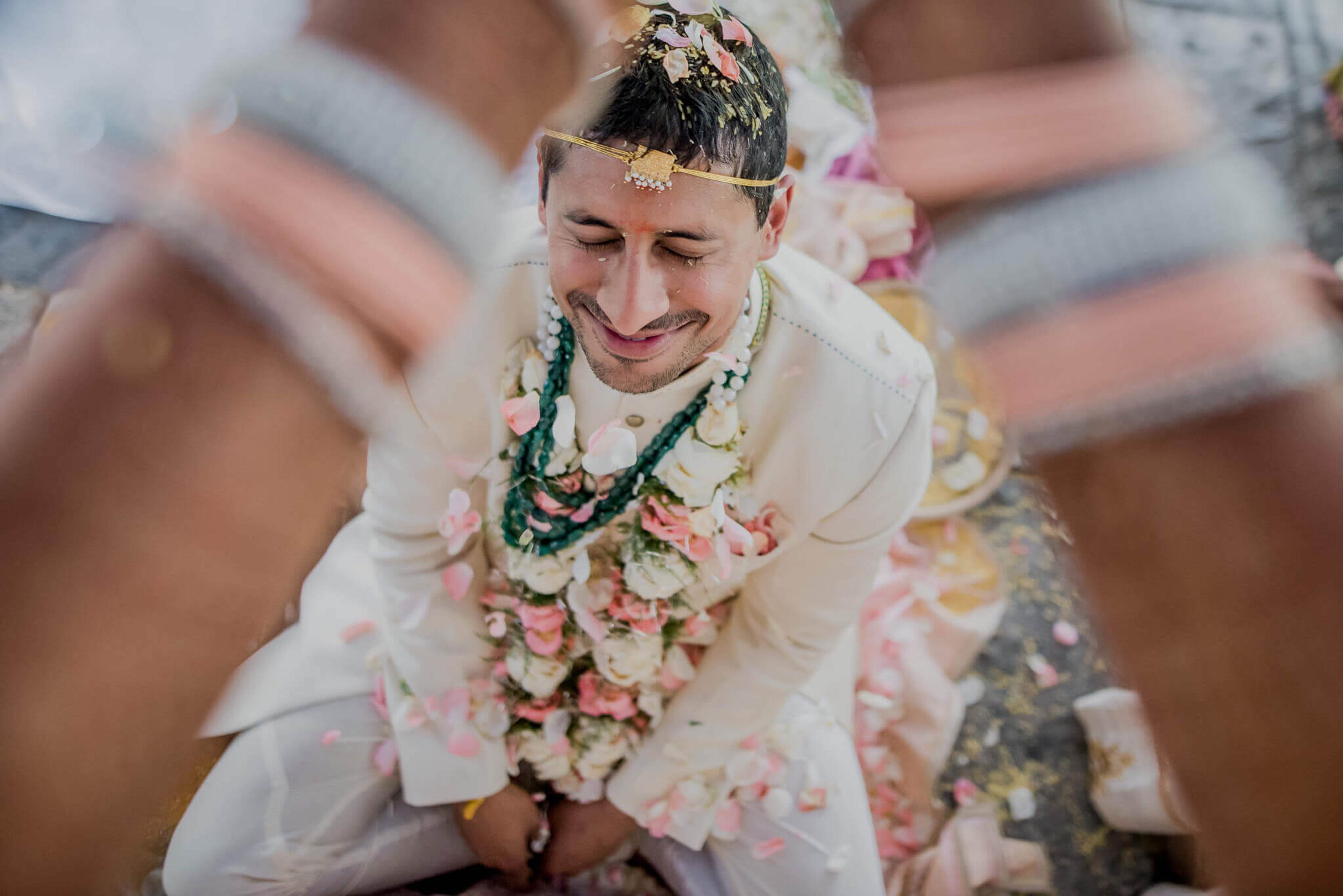 Groom Raghu smiling in white ceremonial attire with floral garland, Nepal wedding celebration