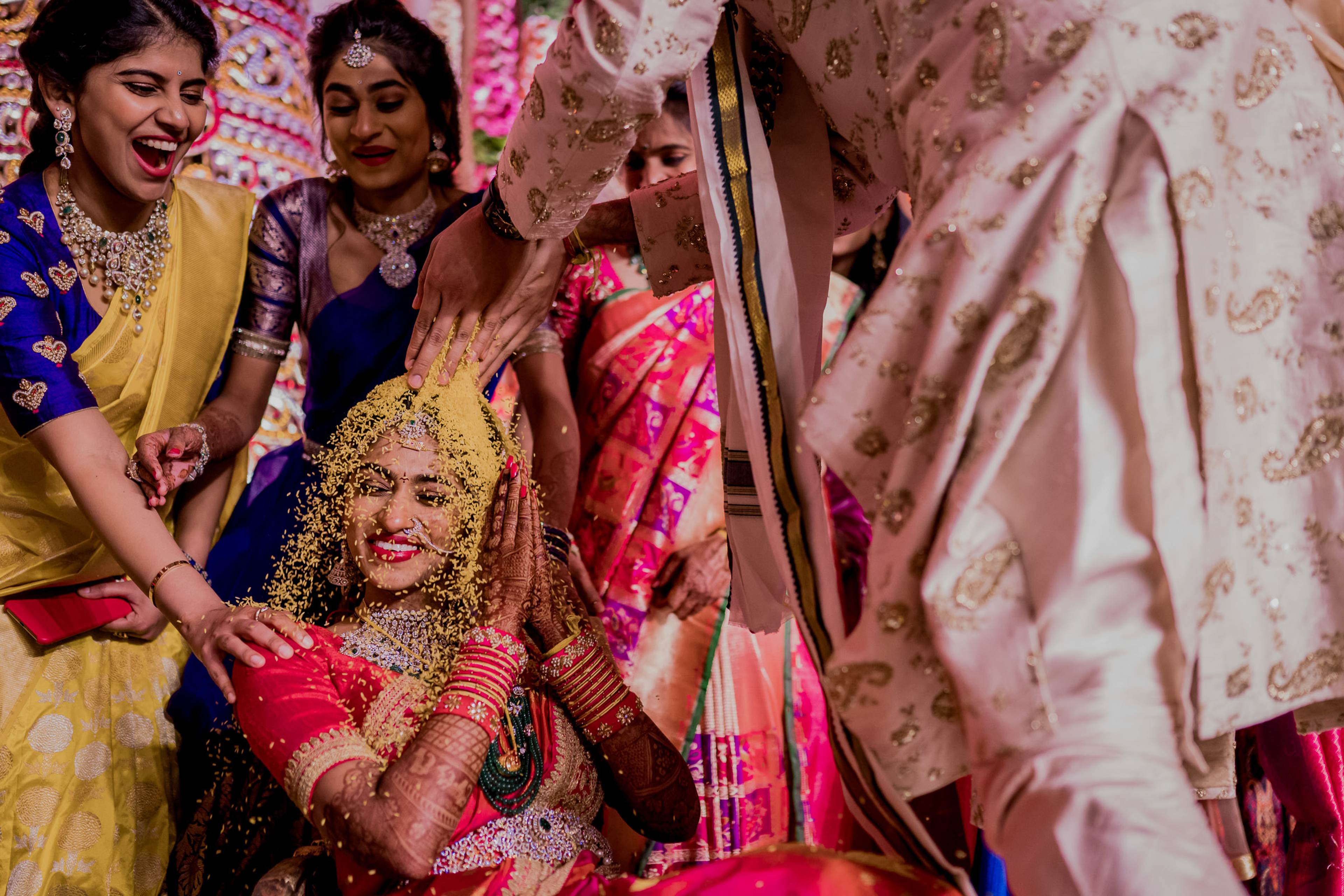 Woman in pink and gold bridal attire surrounded by smiling family members in colorful traditional dress