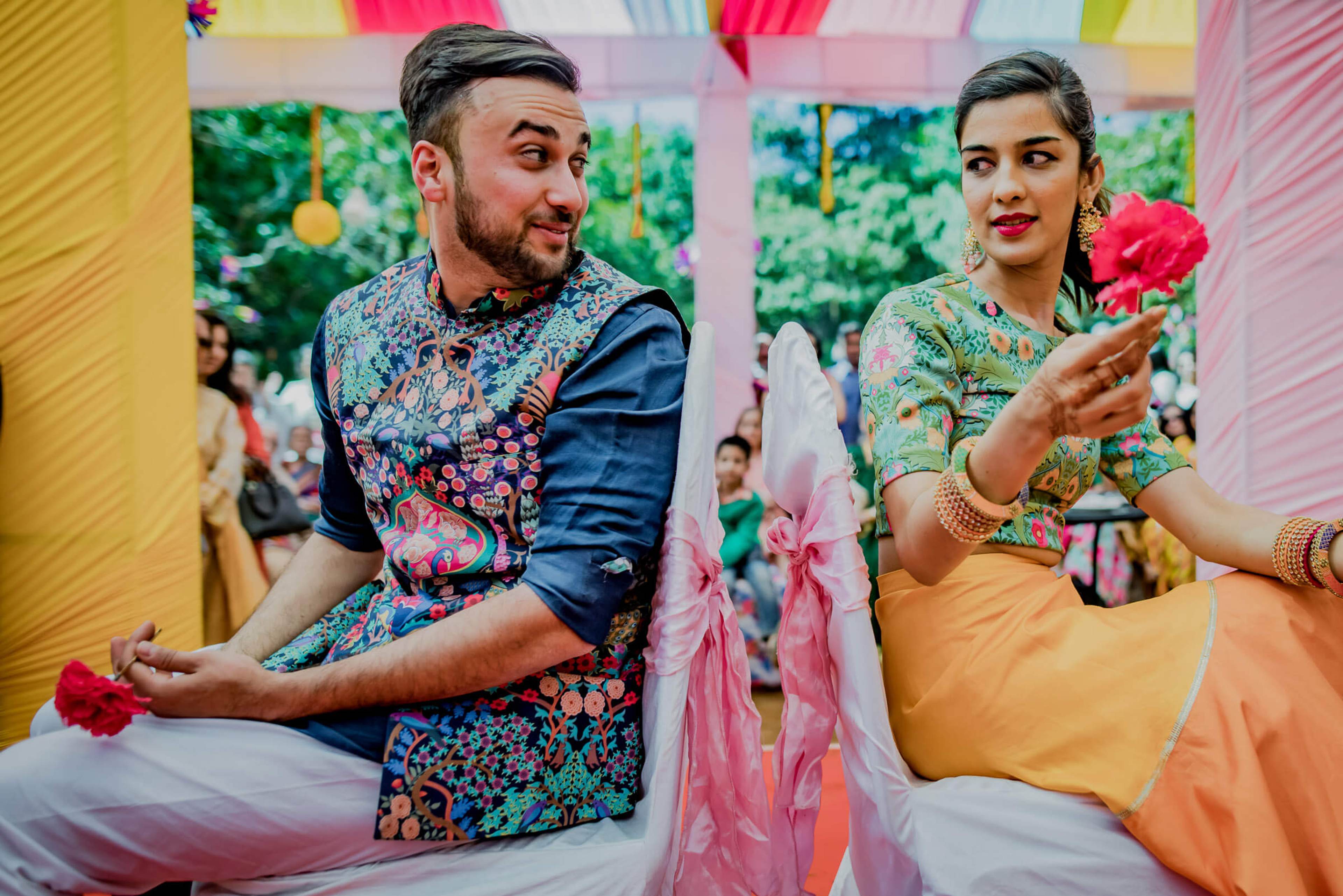 Shreya and Yash hold red flowers at their colorful Mahabaleshwar celebration, surrounded by pink and yellow decorations