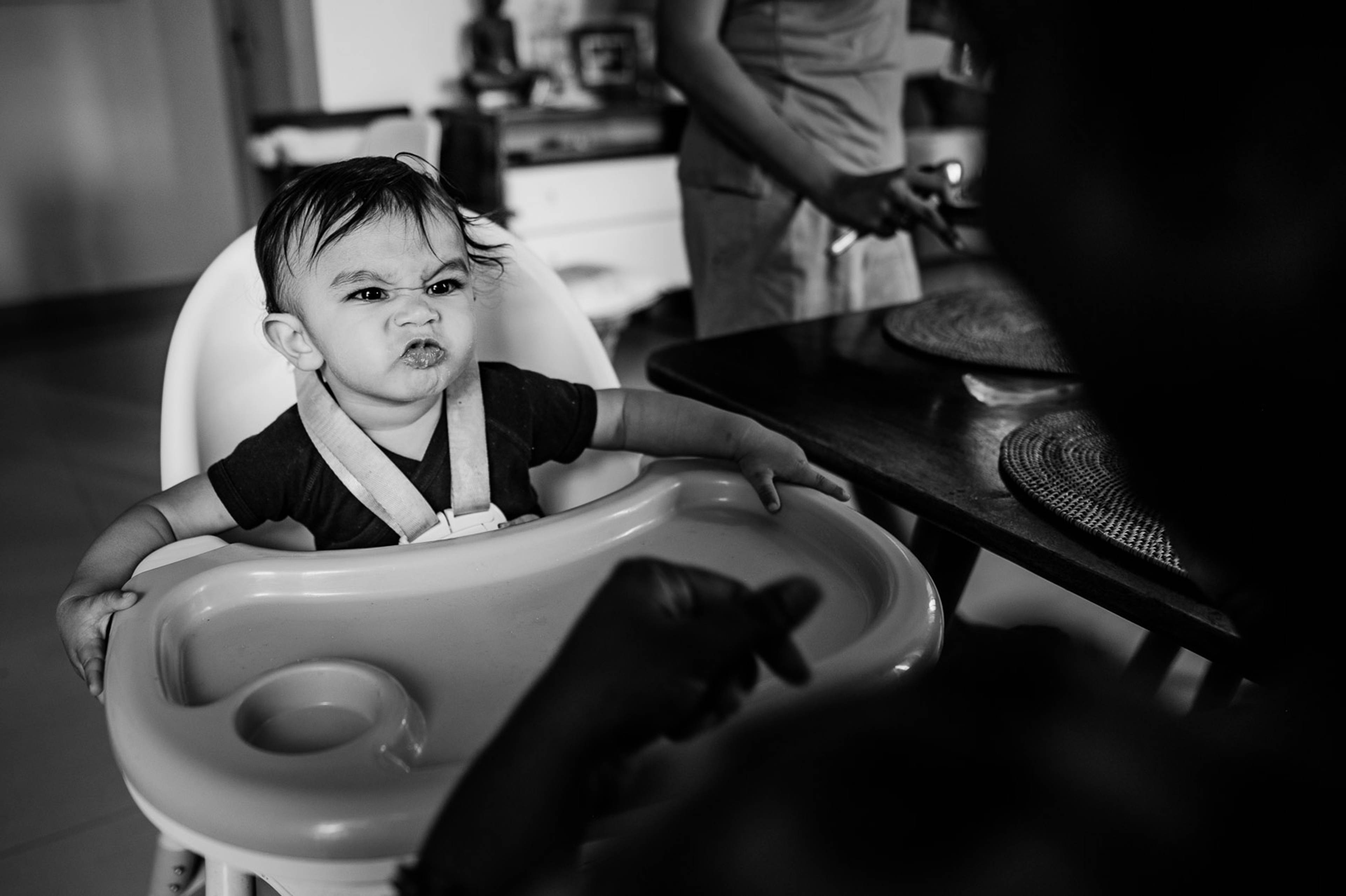 Toddler in high chair during indoor celebration, black-and-white candid moment