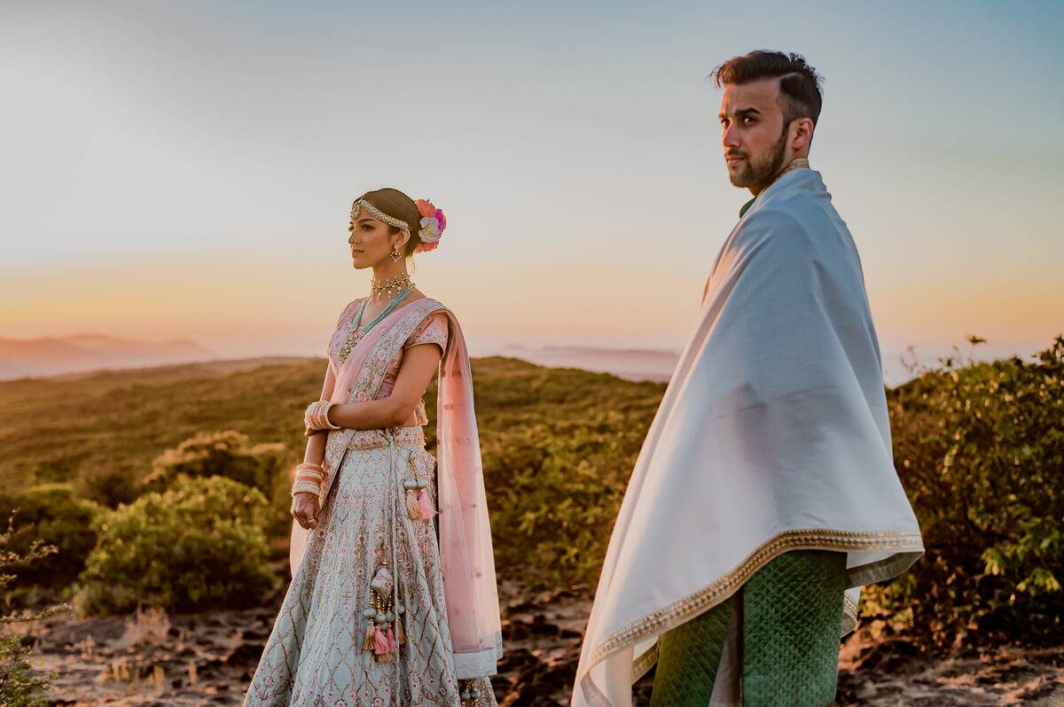 Shreya and Yash stand on a Mahabaleshwar hilltop at sunset, wrapped in flowing fabrics, golden light behind them