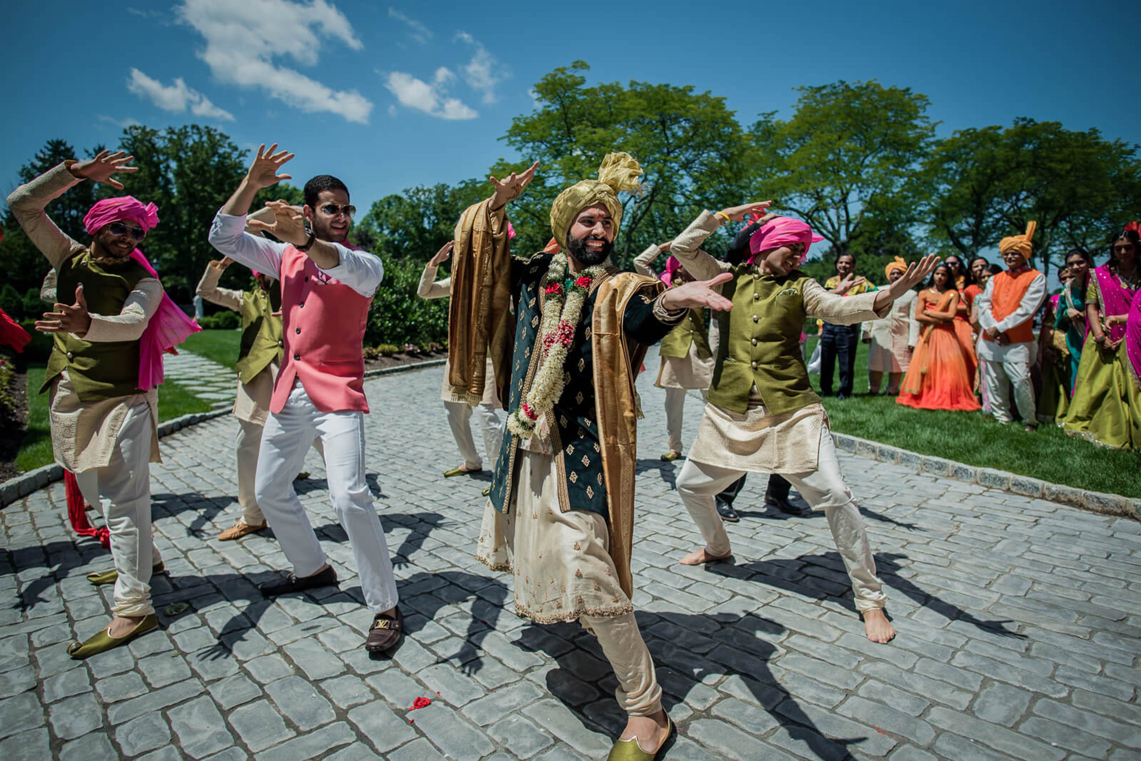 Barkha and Ankit celebrate with joyful dancing and colorful traditional attire in sunny outdoor setting