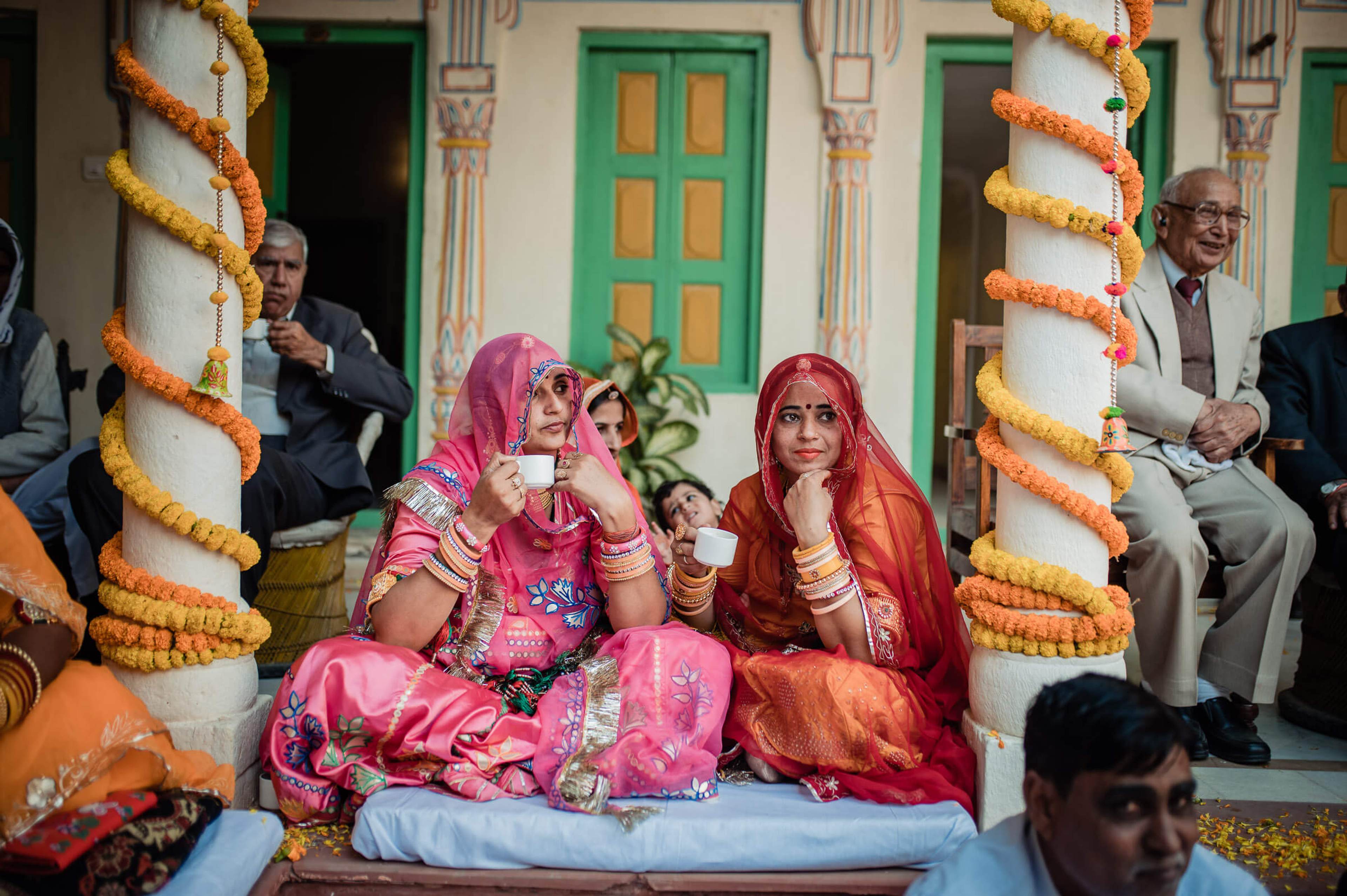 Maitrayee in pink bridal attire with family in Rajasthan courtyard framed by marigold garlands