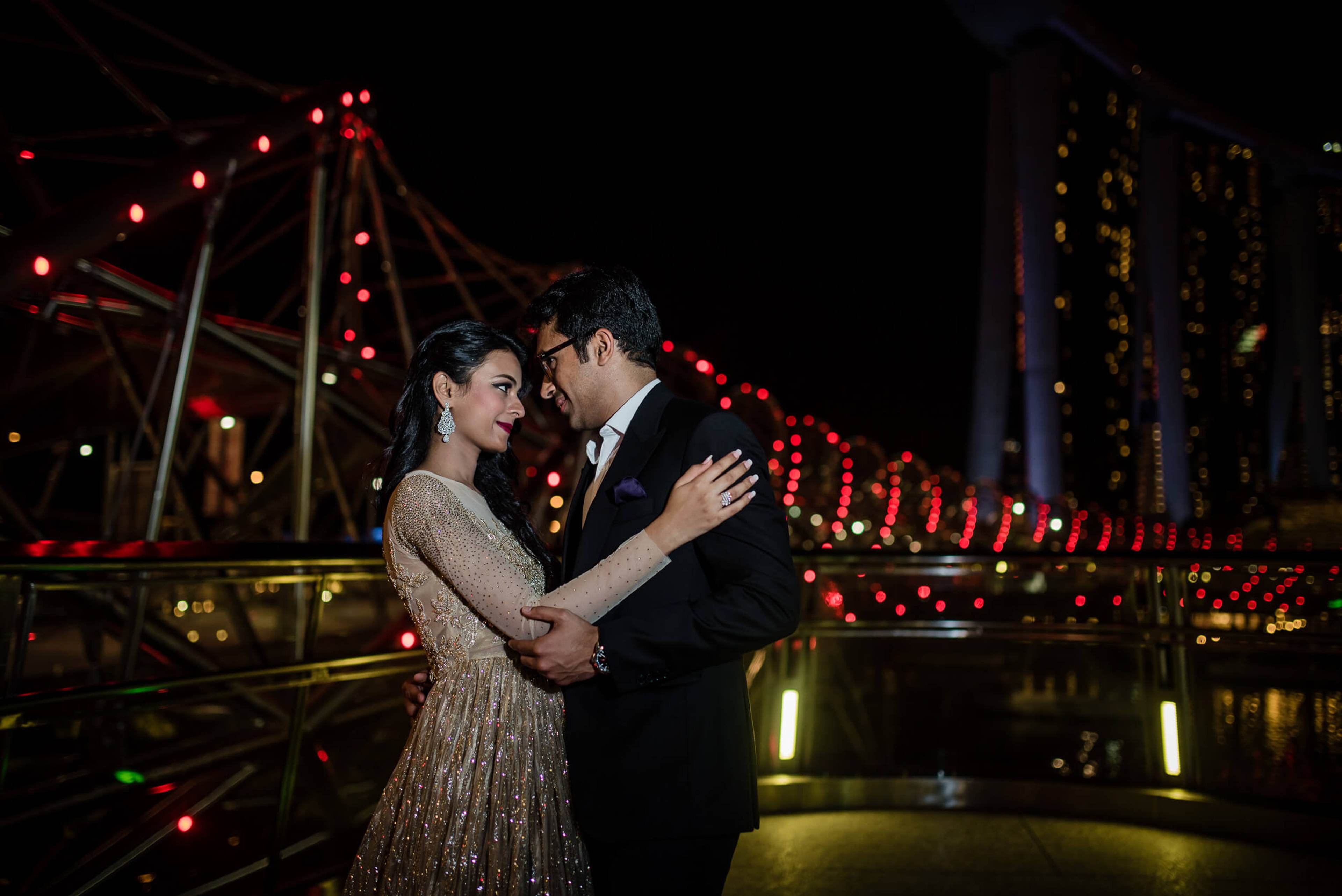 Yash and Disha embrace under glowing carnival lights at night in Singapore