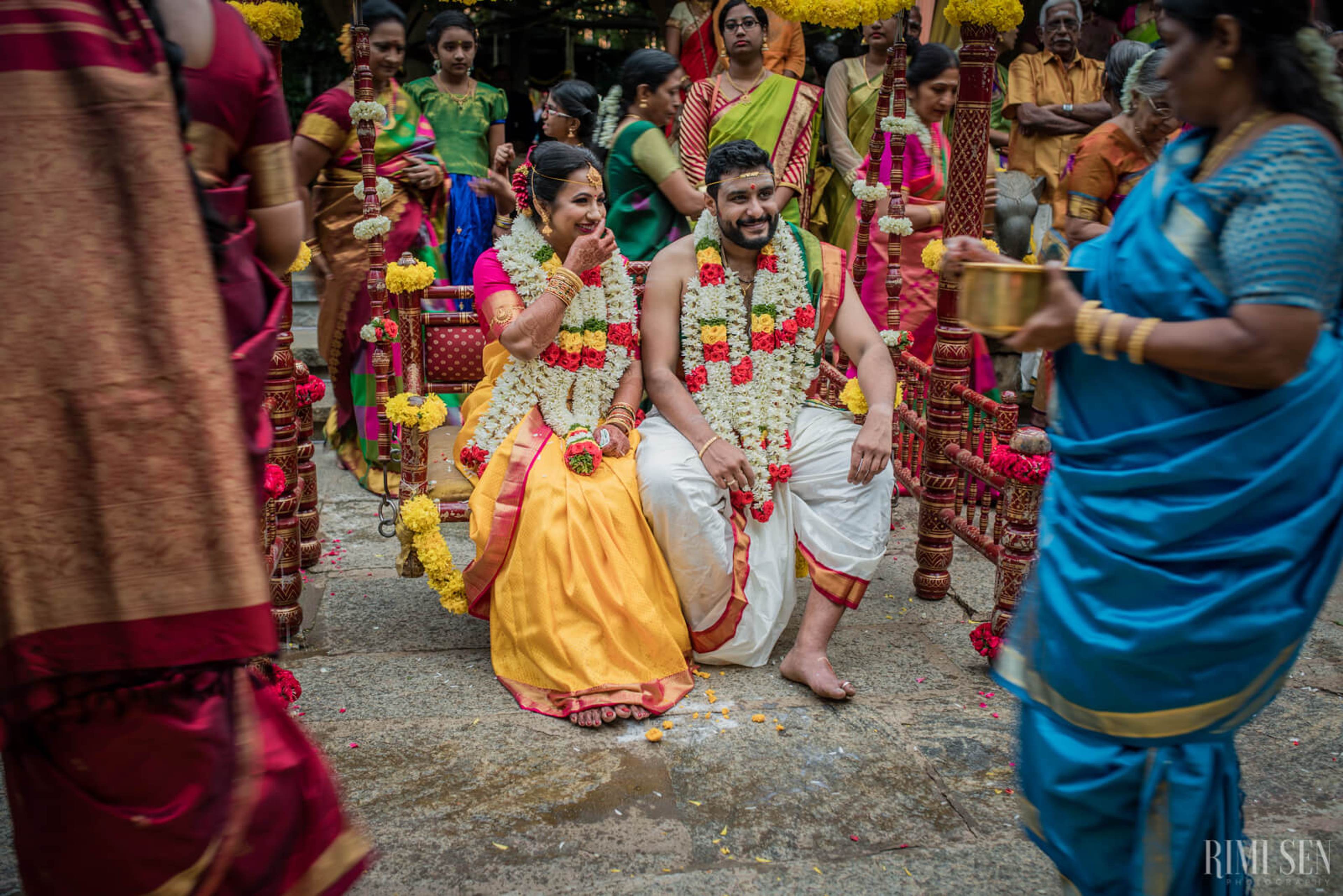 Nivetha and Sridhar wearing flower garlands and traditional attire surrounded by colorful guests at their Bangalore wedding ceremony