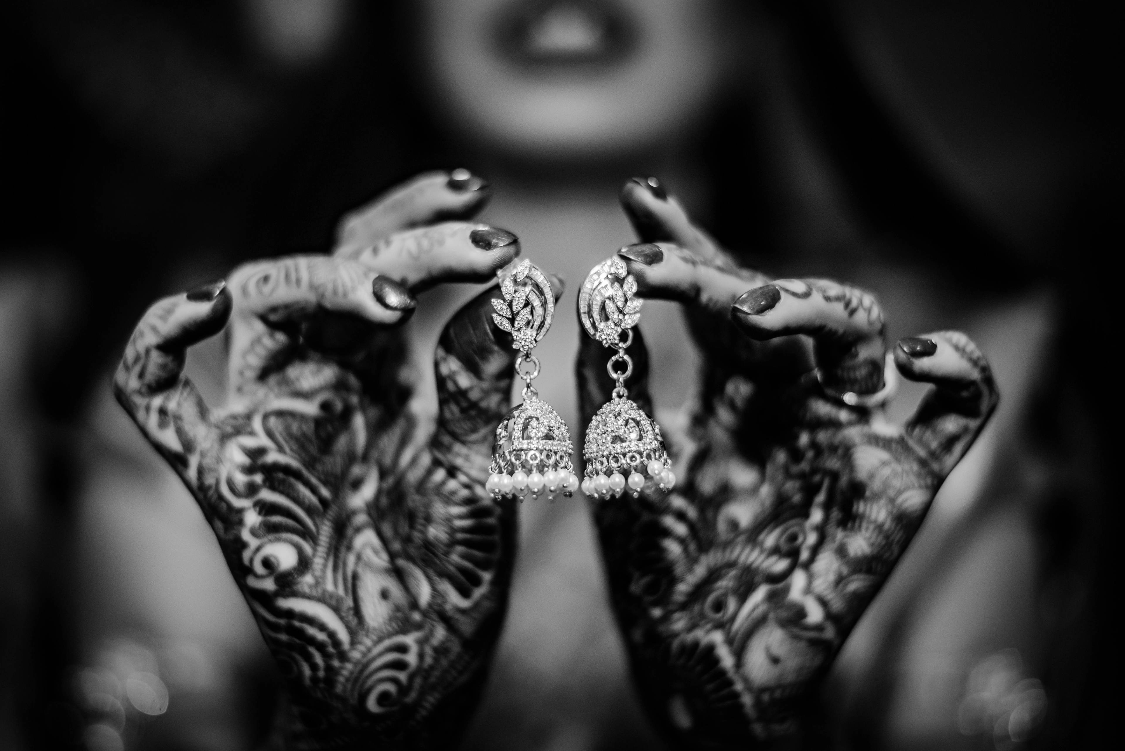 Hands with henna and ornate jeweled earrings displayed in black and white detail shot