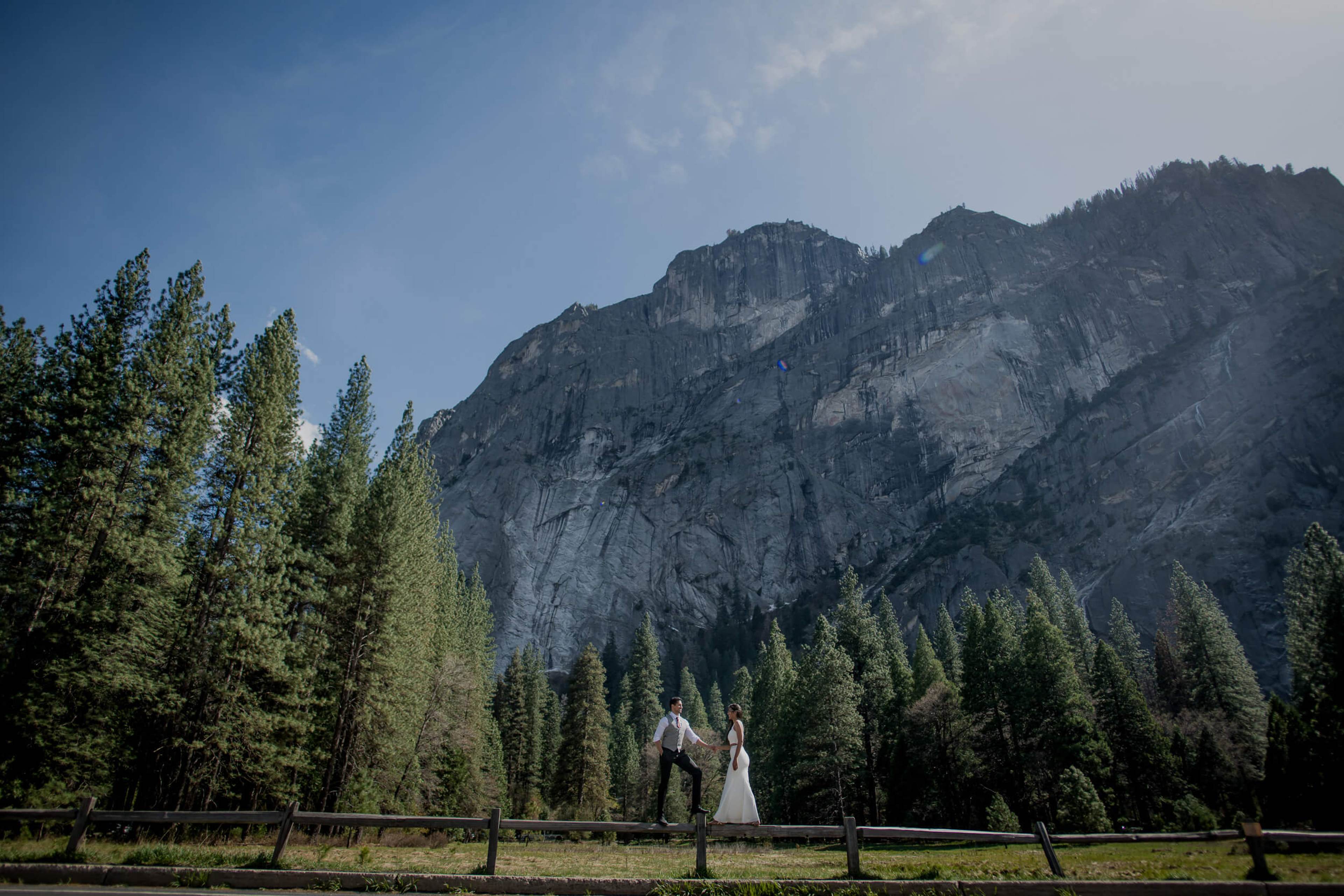 Anu and Raghu standing at a wooden fence with towering granite cliffs and pine forest behind them in California