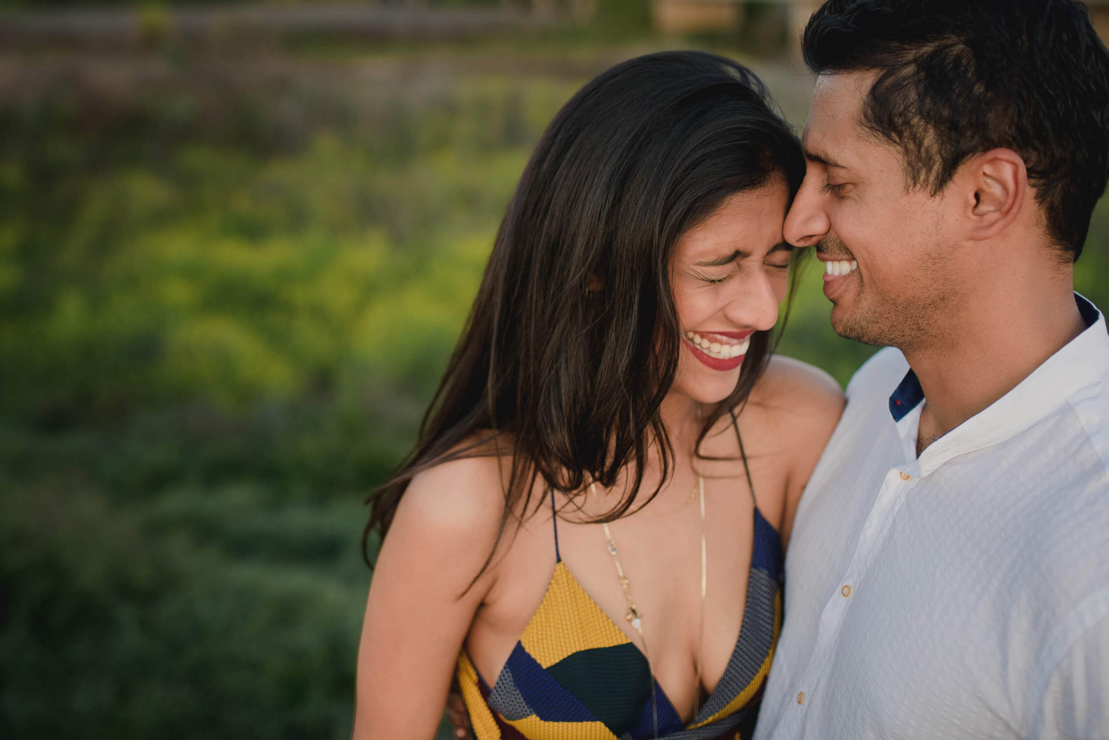 Anu and Raghu smile together outdoors in California, soft natural light, lush green background