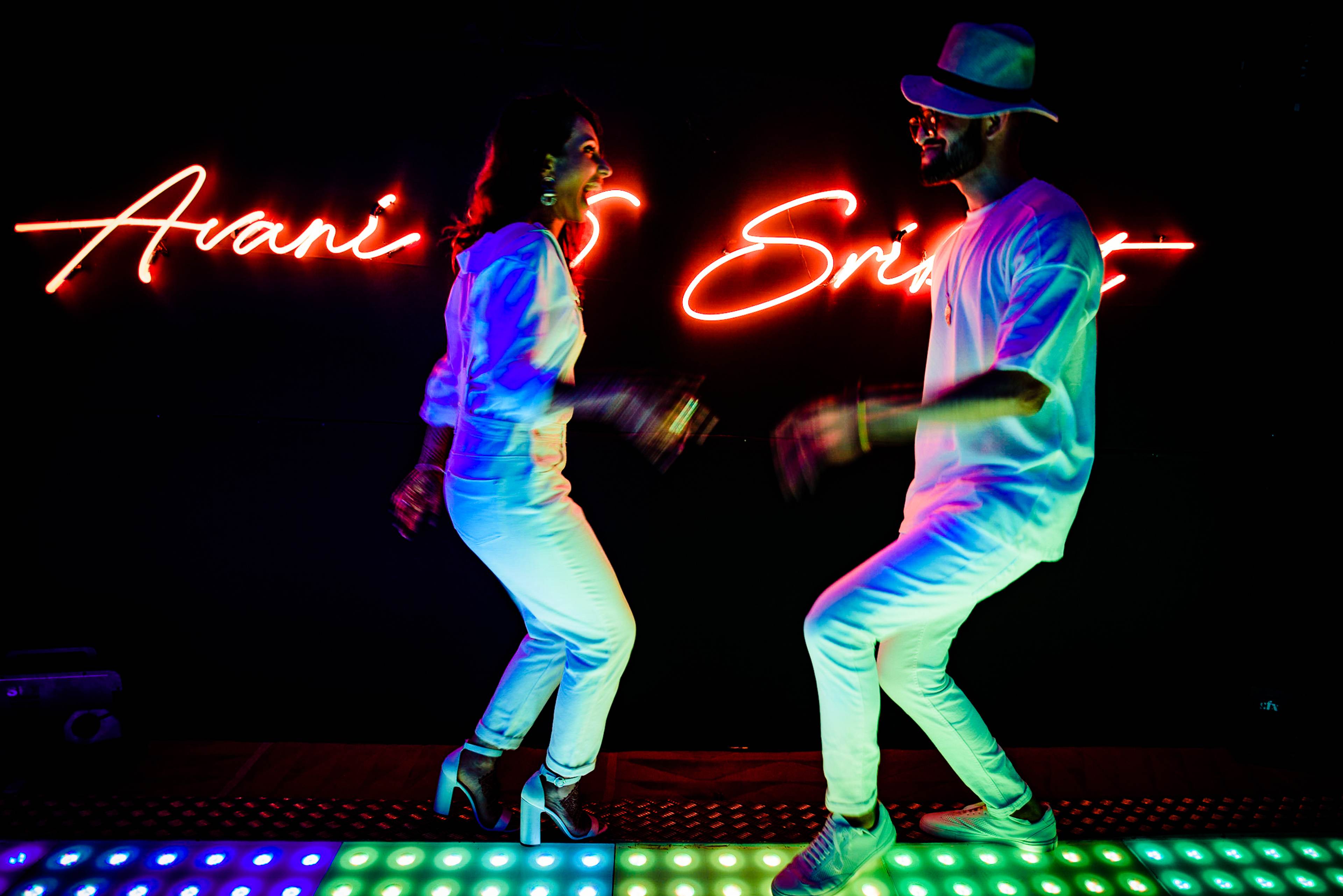 Avani and Srikant dancing under neon lights with colorful glow effects at night