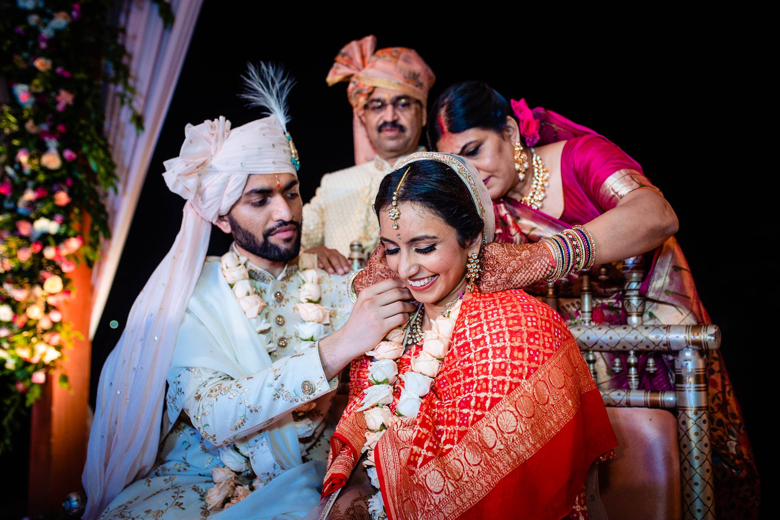 Avani and Srikant in traditional wedding attire surrounded by family during ceremony in Goa, vibrant floral backdrop