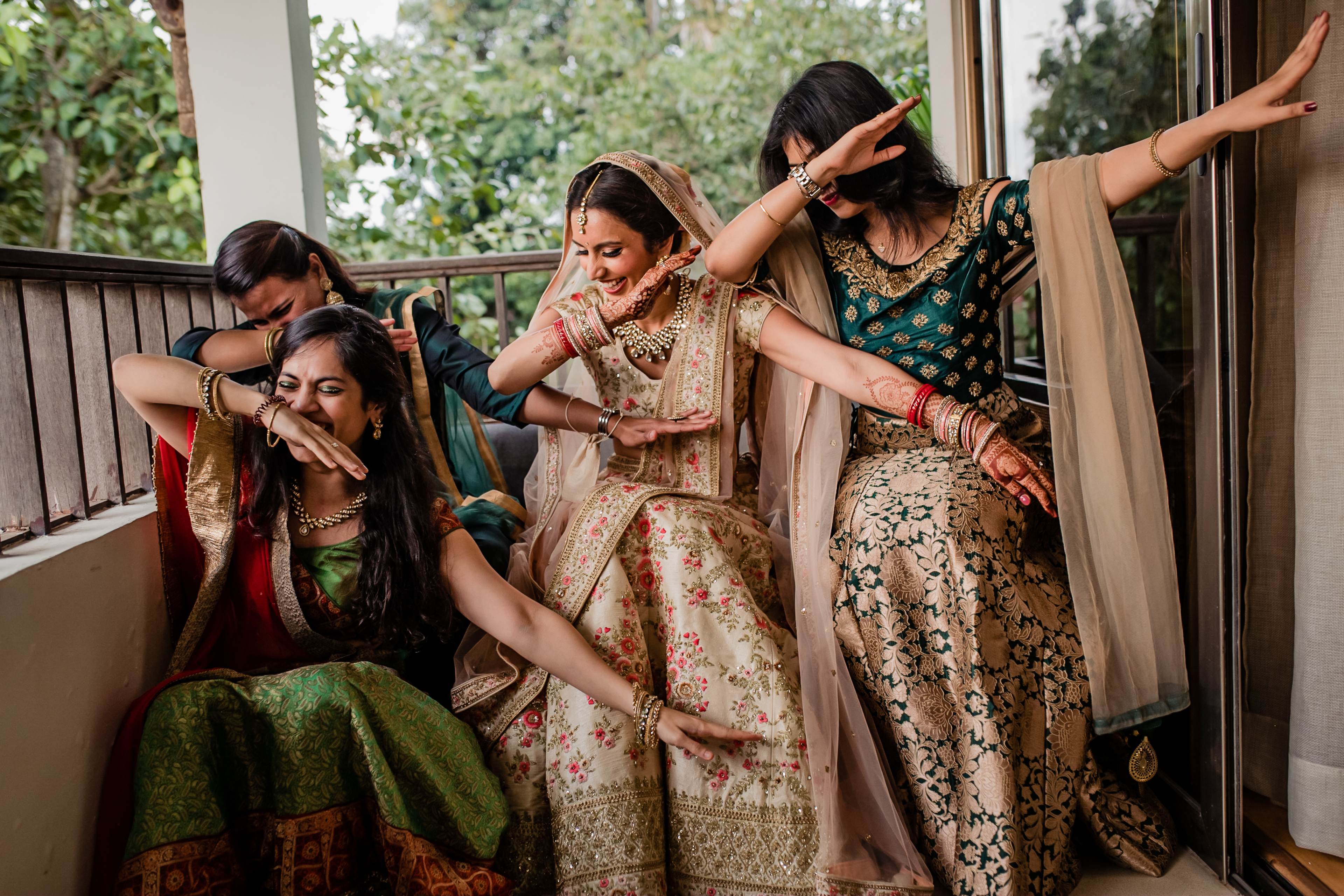 Four women in traditional Indian attire laughing and posing together on a sunlit balcony in Goa